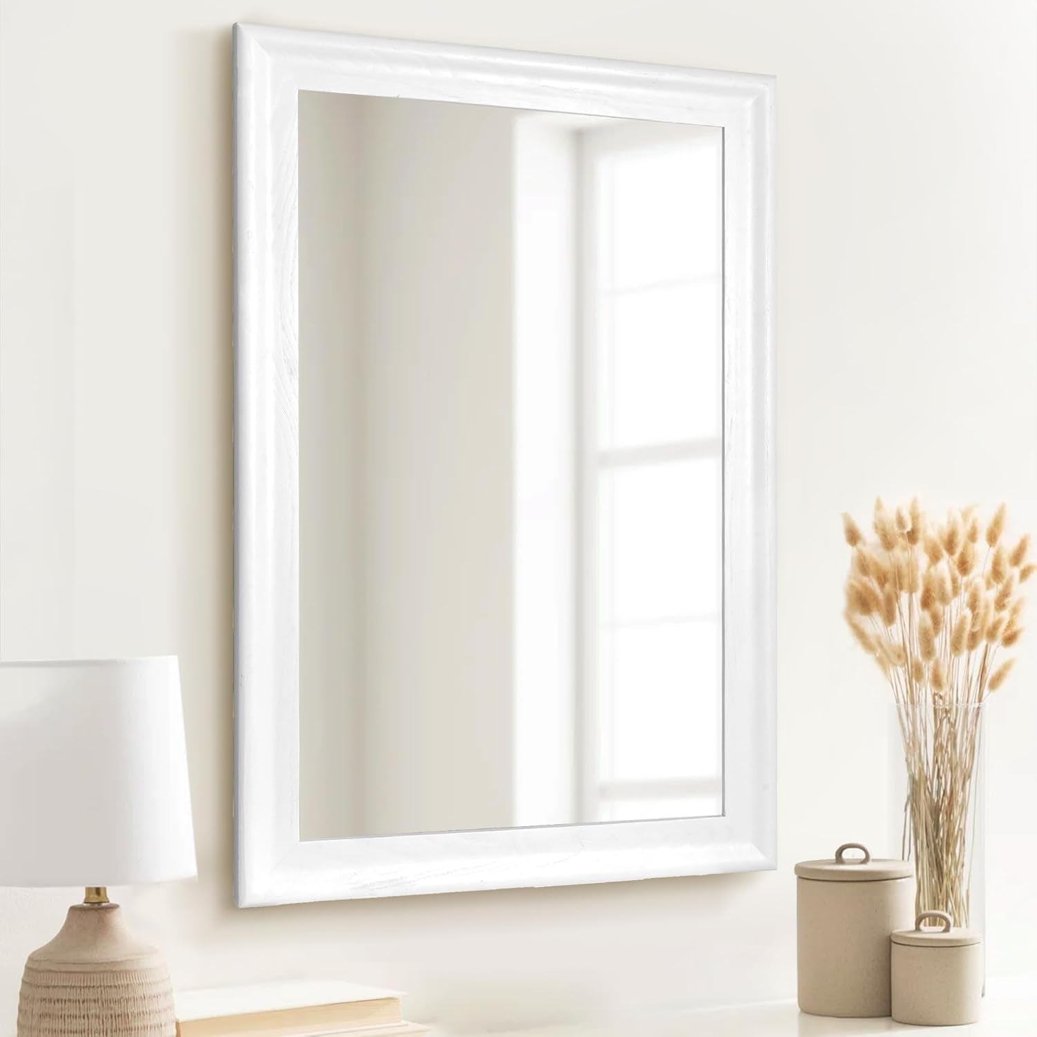 White-framed mirror on a white wall with decorative items below.
