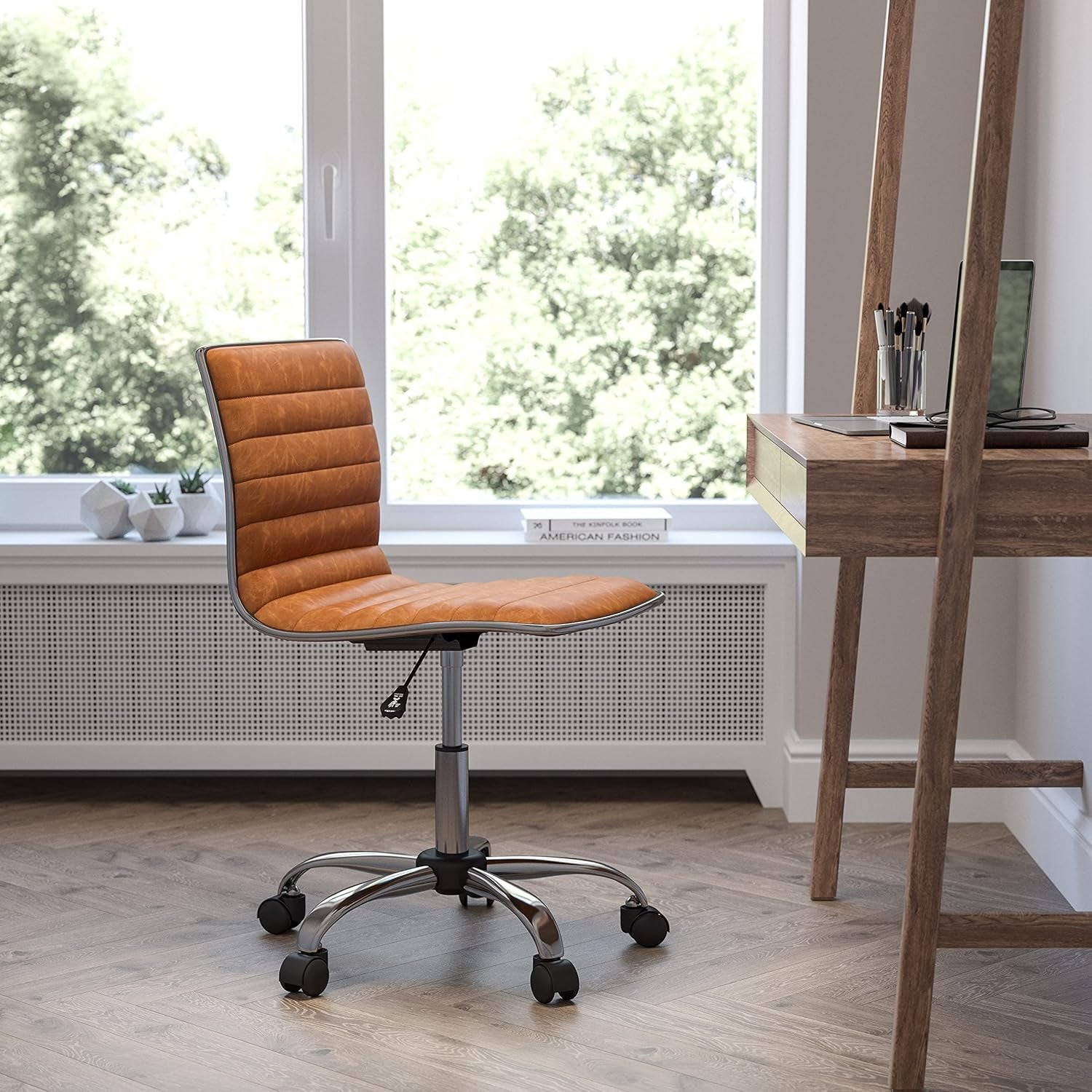 Brown office chair in front of a wooden desk with a laptop in a bright room with large windows.