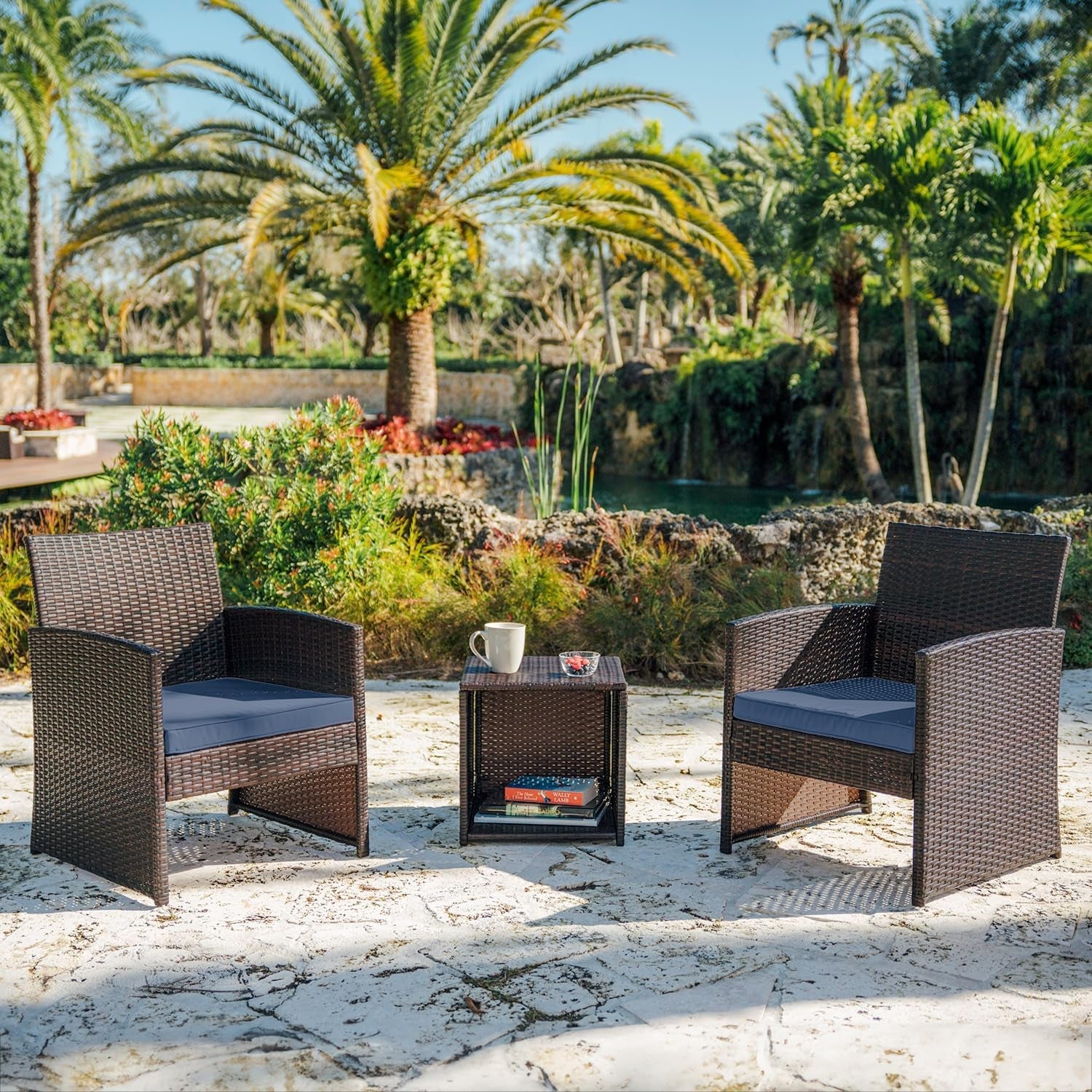Outdoor patio set with two chairs and a table on a stone patio with palm trees in the background.
