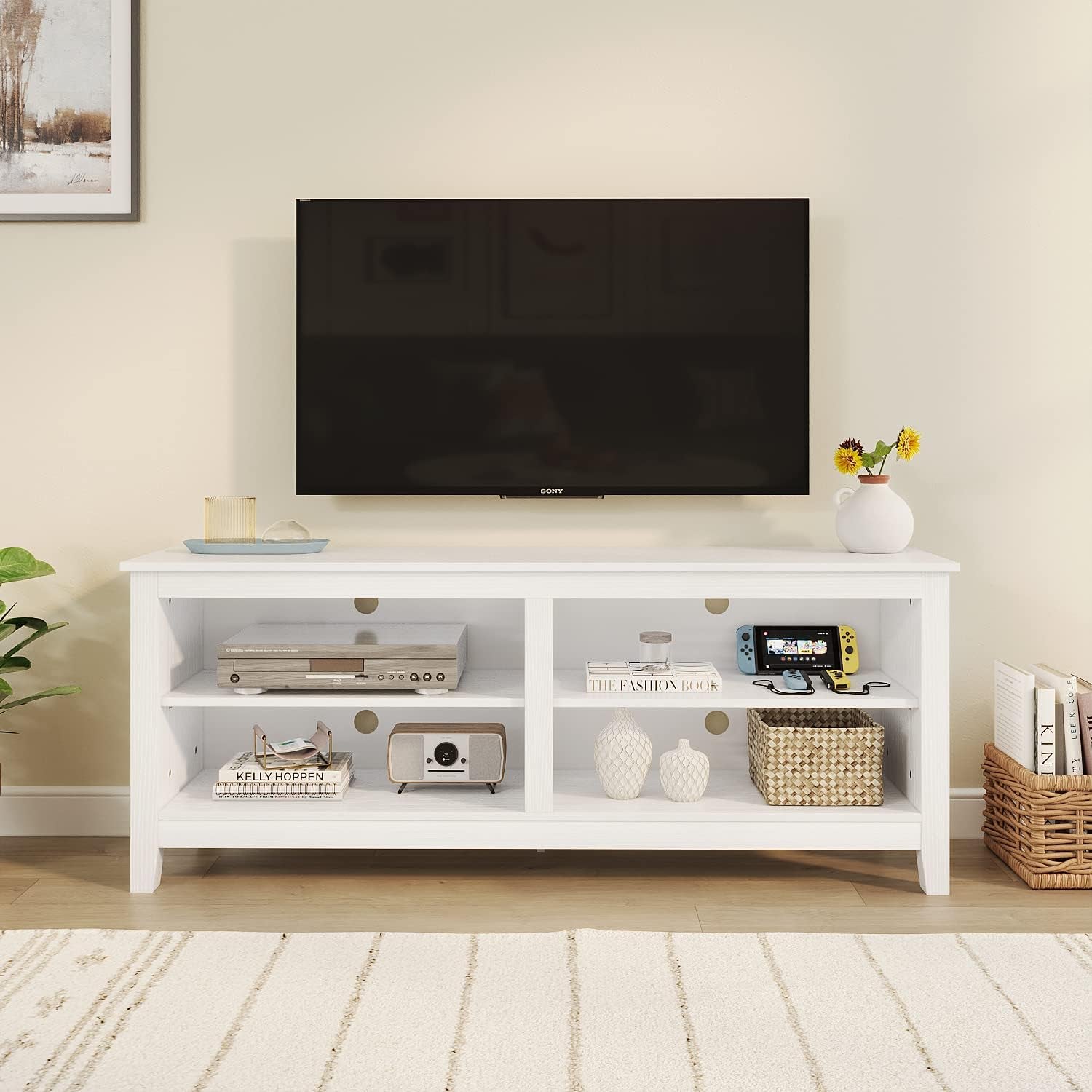 White TV stand with electronic devices and decor items against a beige wall.