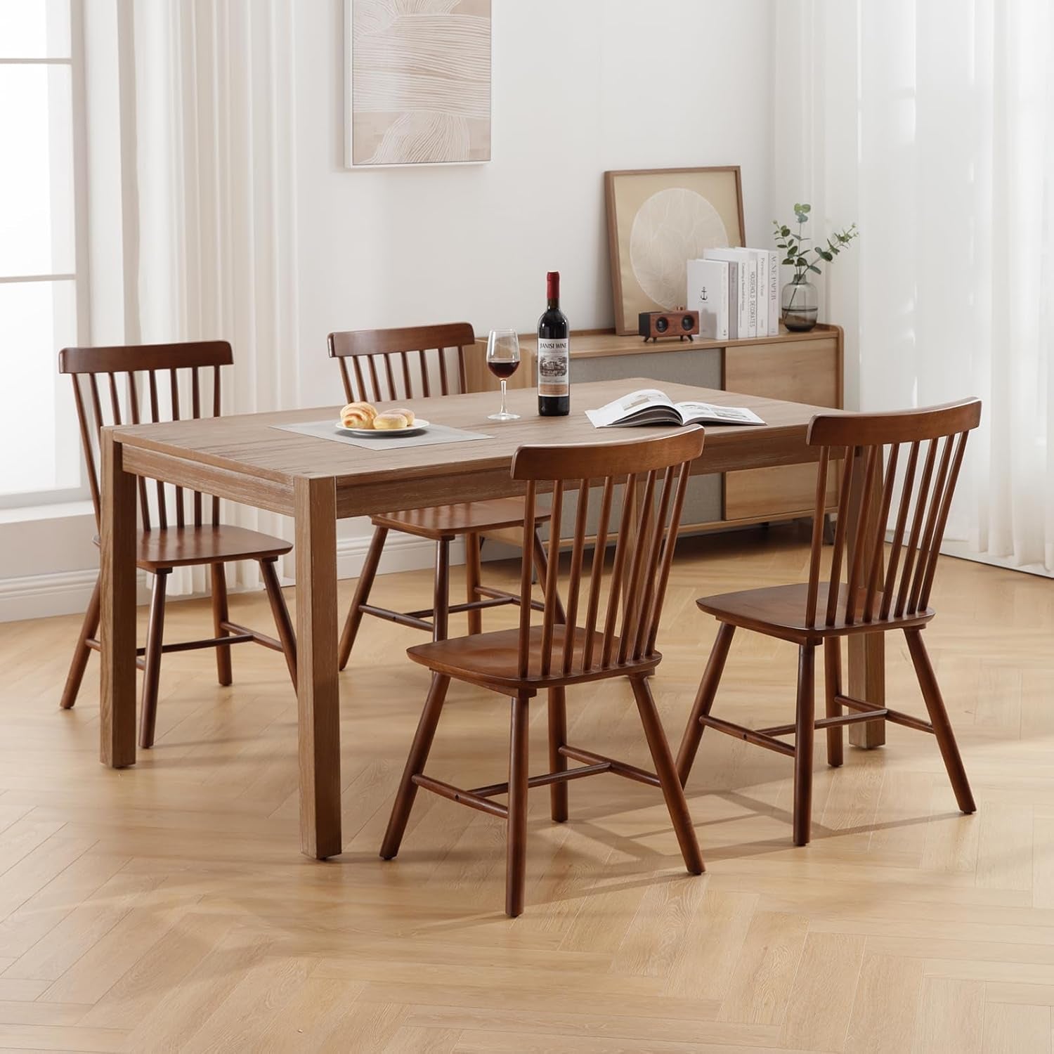 Wooden dining table with four chairs in a room with light-colored walls and flooring.