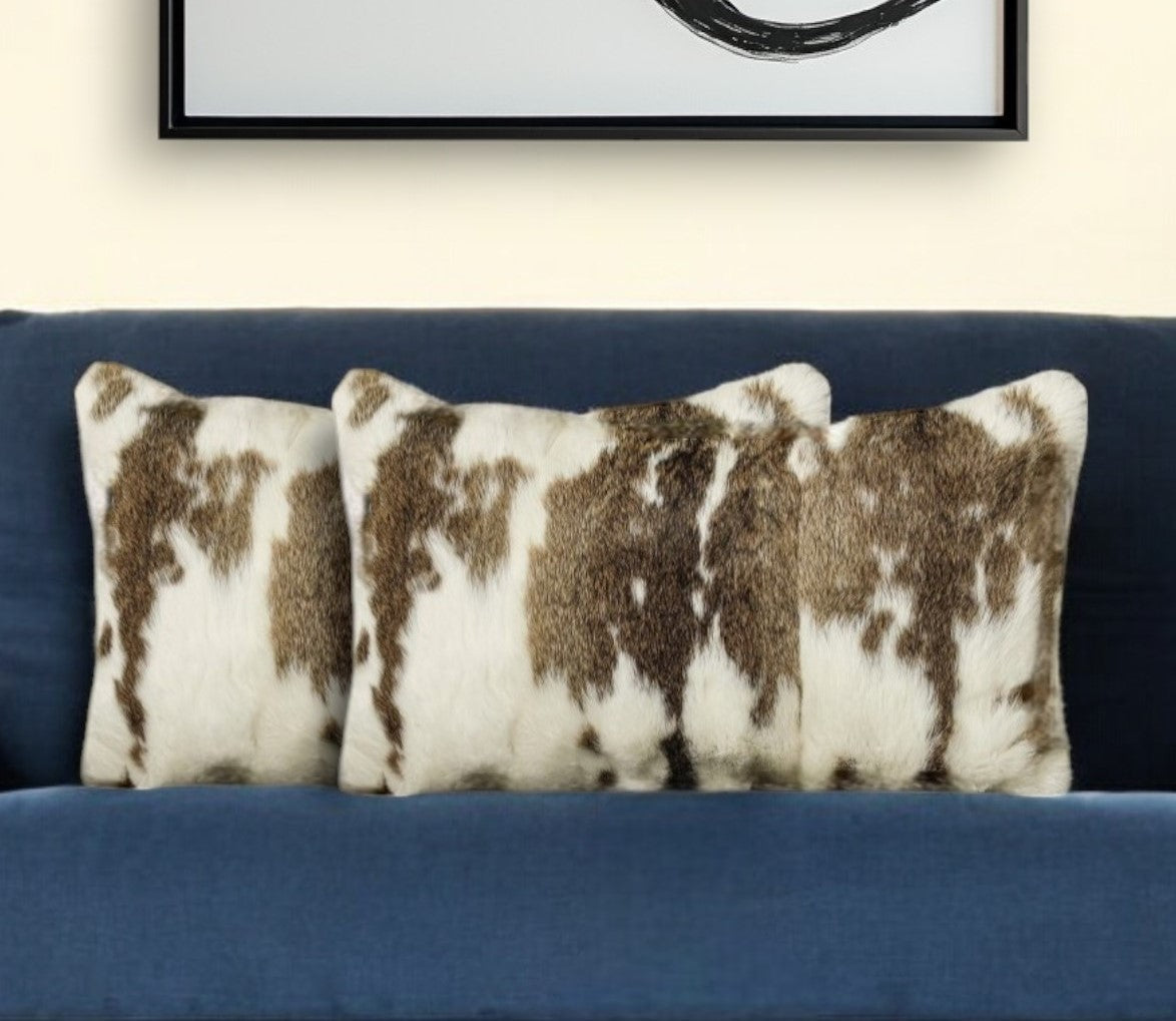 Three cowhide patterned pillows on a blue couch with a framed picture in the background.