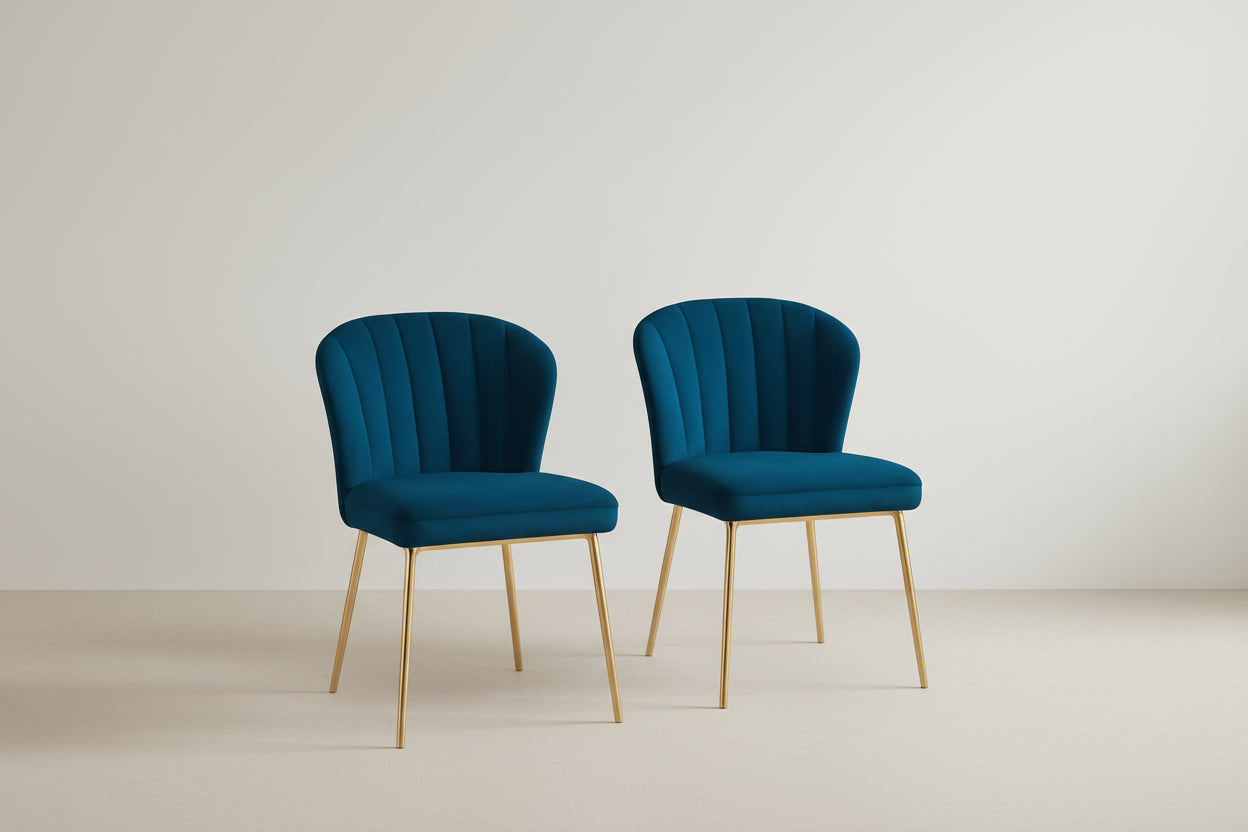 Two blue velvet chairs with gold legs in a room with a beige wall and wooden floor.