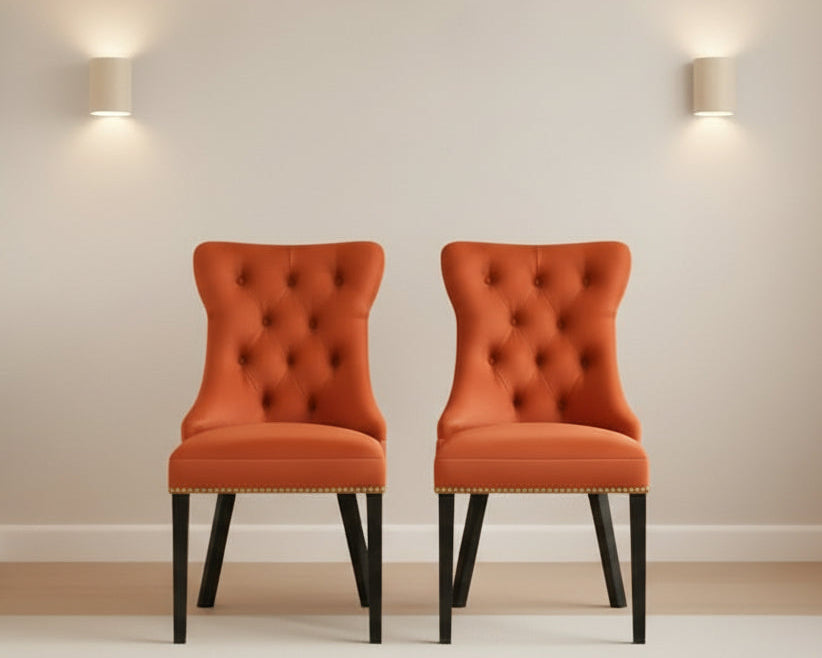 Two orange tufted chairs in a room with a peach wall and decorative items.