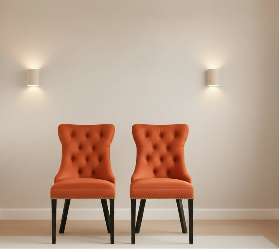 Two orange tufted chairs in a room with a peach wall and decorative items.