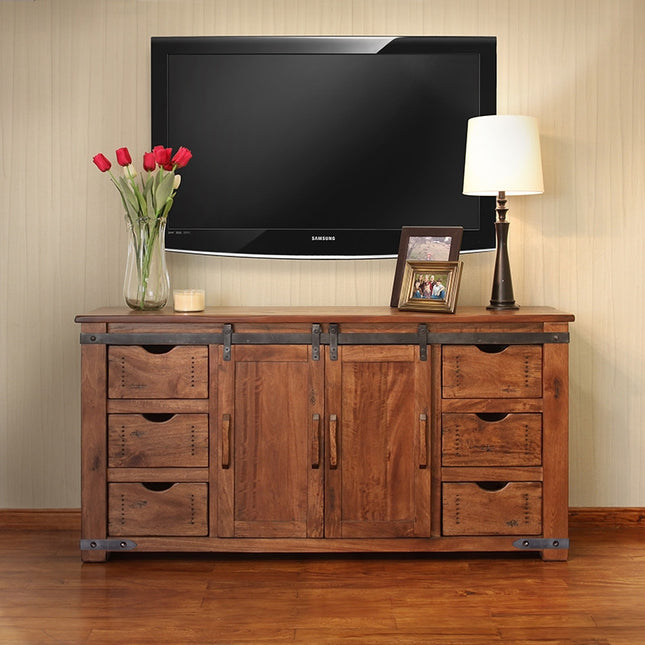 Wooden entertainment console with TV above, flowers, and lamp in a room.