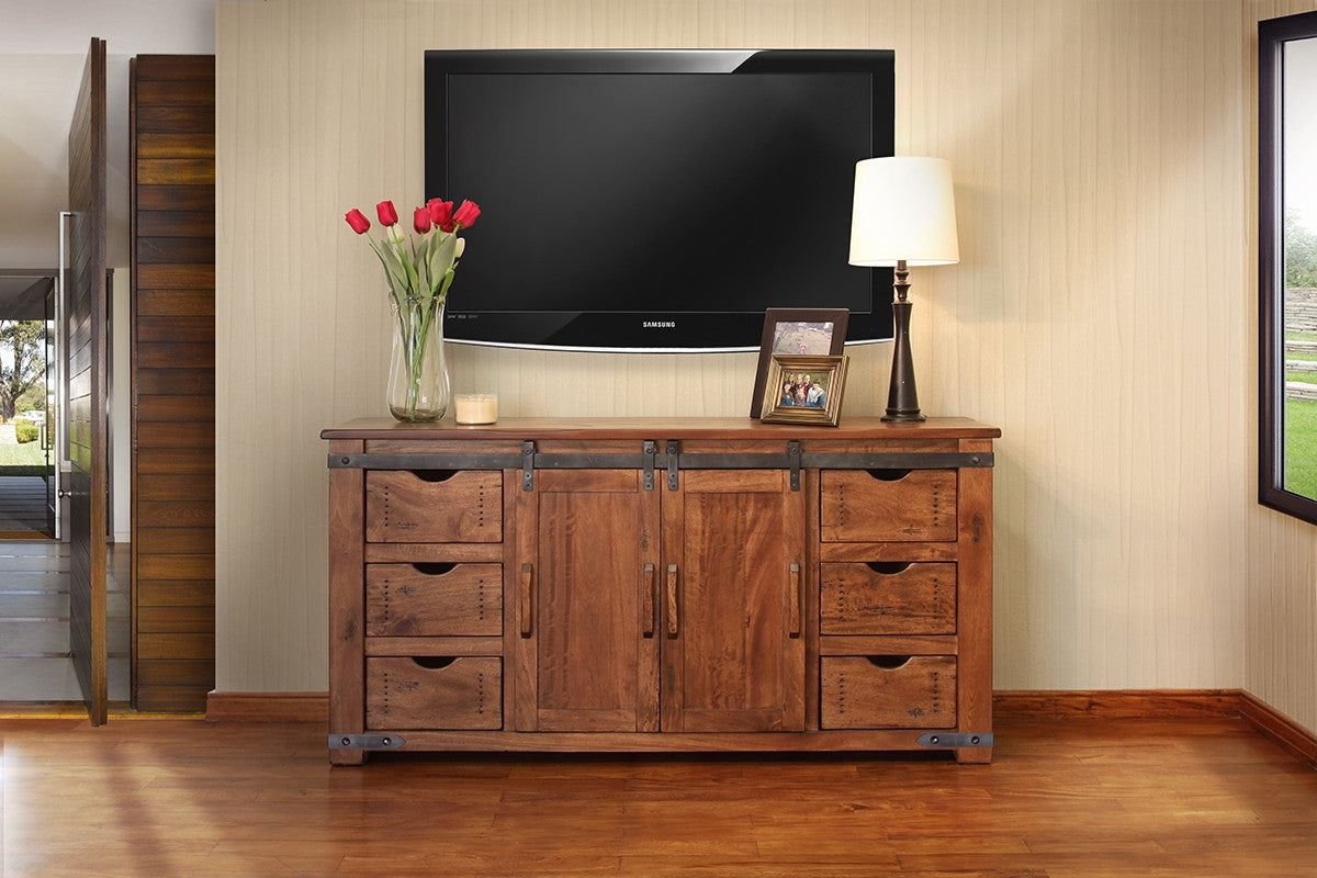 Wooden entertainment console with TV above, flowers, and lamp in a room.