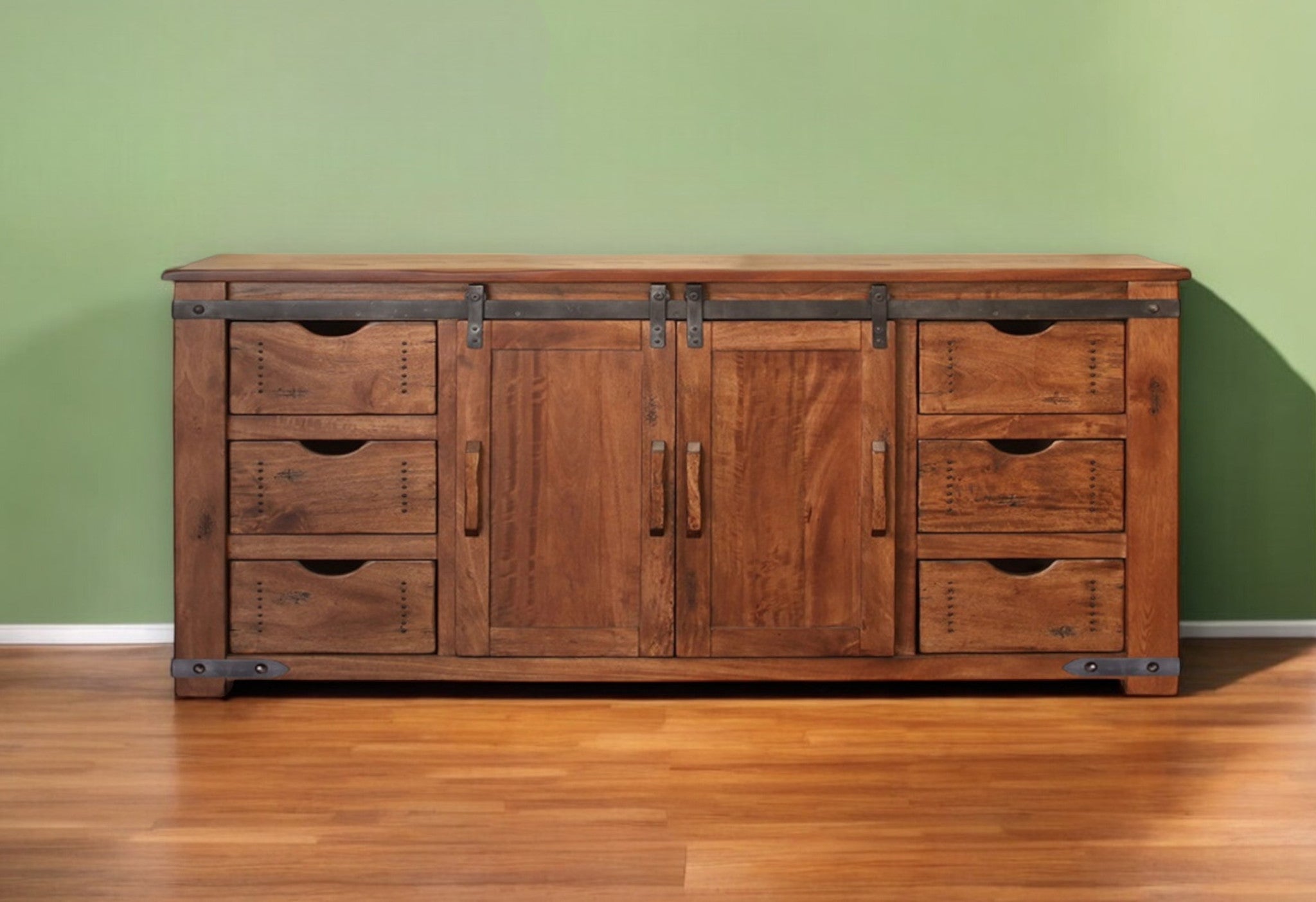 Wooden dresser with multiple drawers and doors against a green wall.