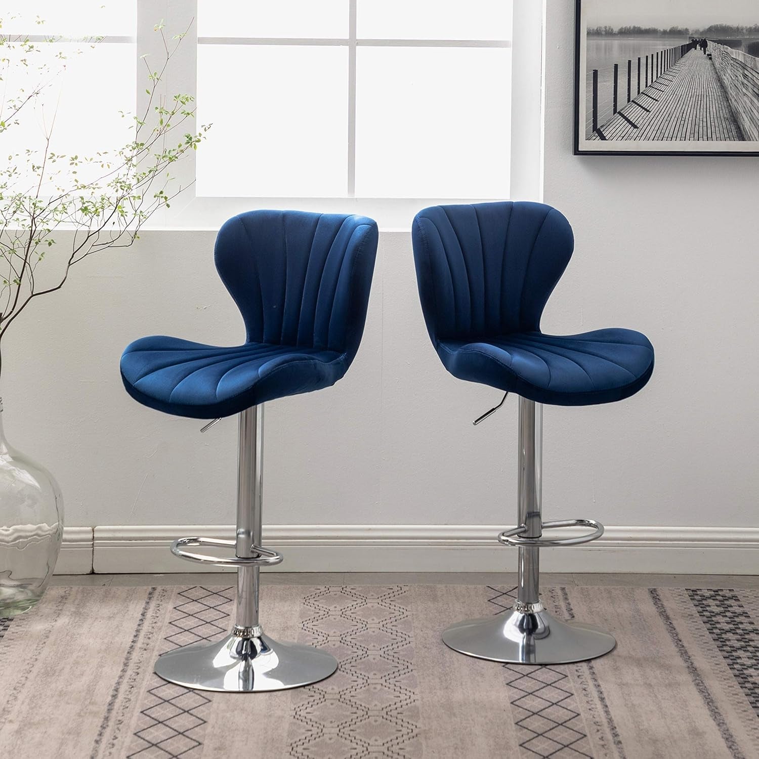 Two blue bar stools with chrome bases in a room with a window and framed picture.