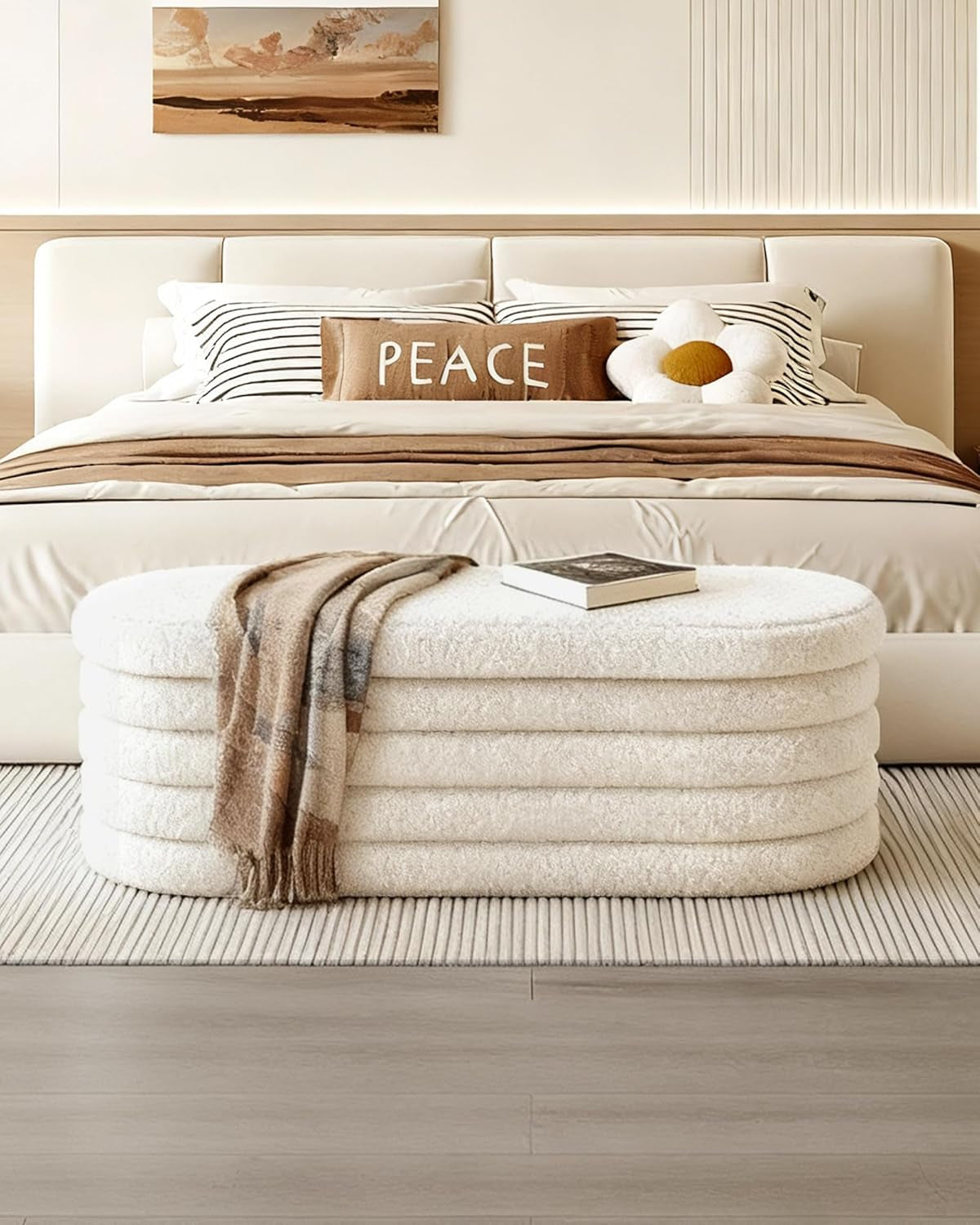 Beige ottoman with a blanket on top in front of a bed with pillows and a 'PEACE' sign.