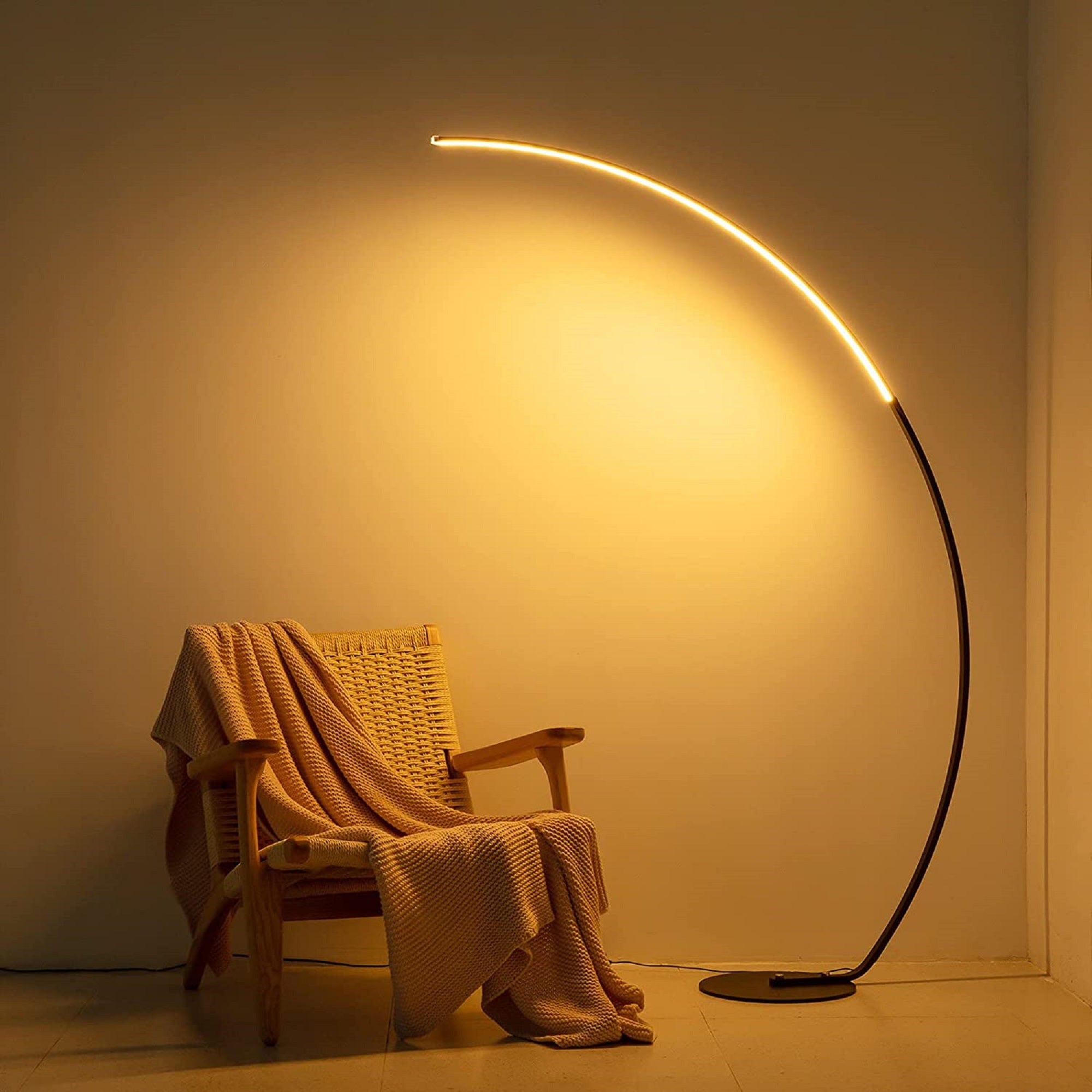 Curved floor lamp casting a warm glow on a chair with a blanket in a room.