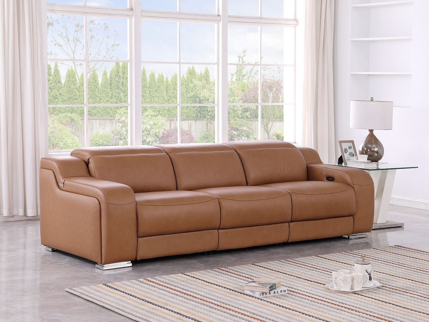 Brown leather sofa in a living room with large windows and a striped rug.