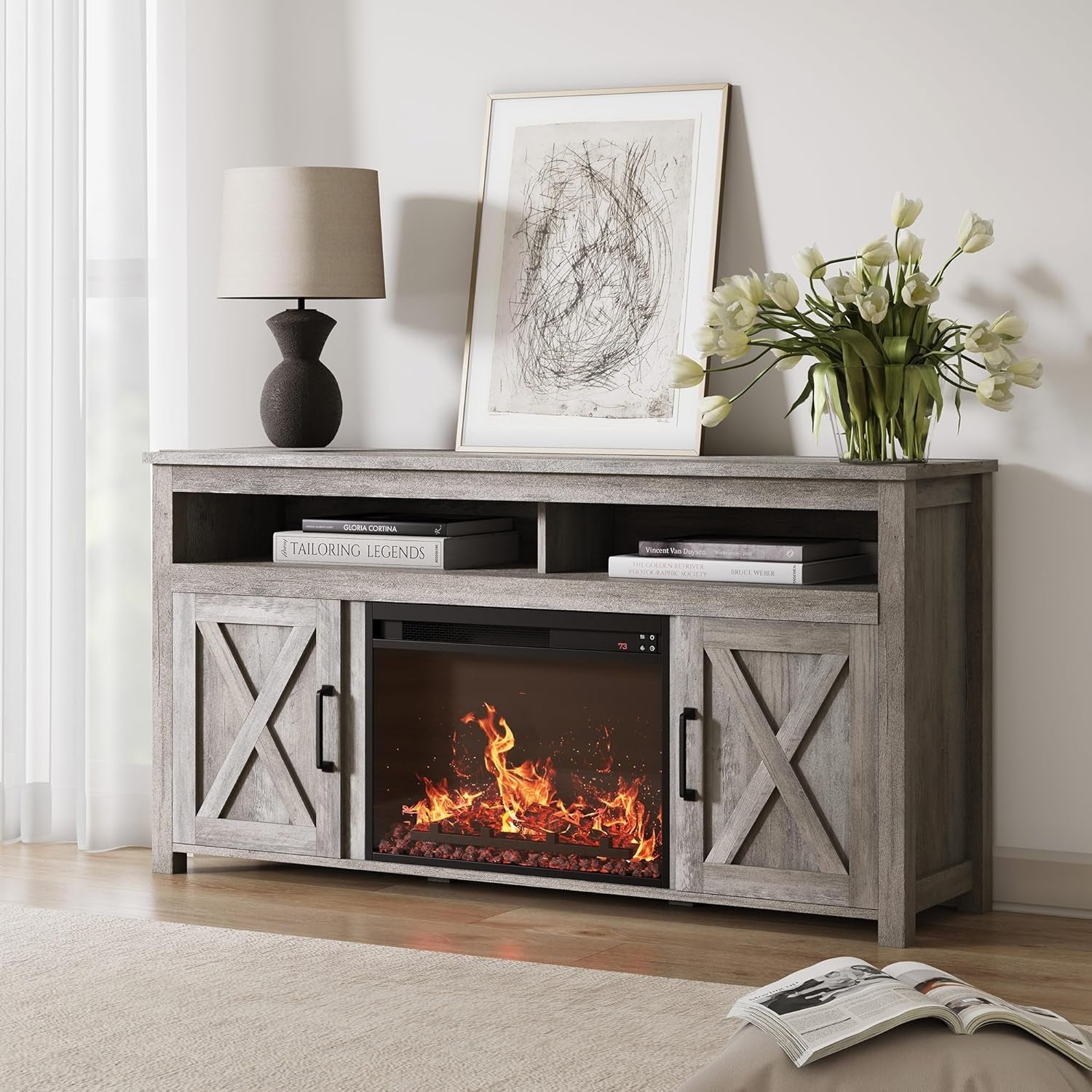 Wooden entertainment console with electric fireplace, lamp, and flowers in a living room setting.