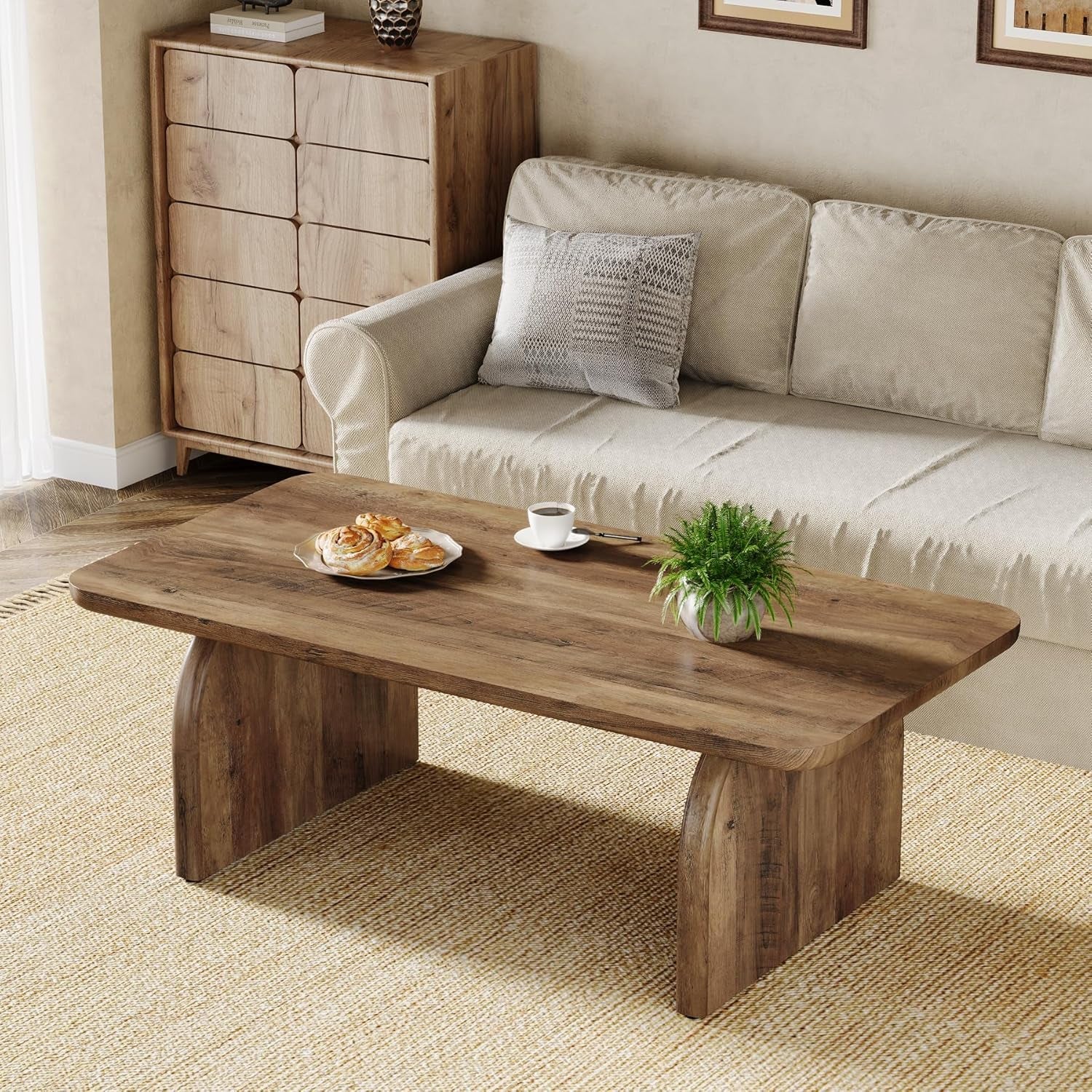 Wooden coffee table with a plate of pastries, cup of coffee, and plant in a living room setting.