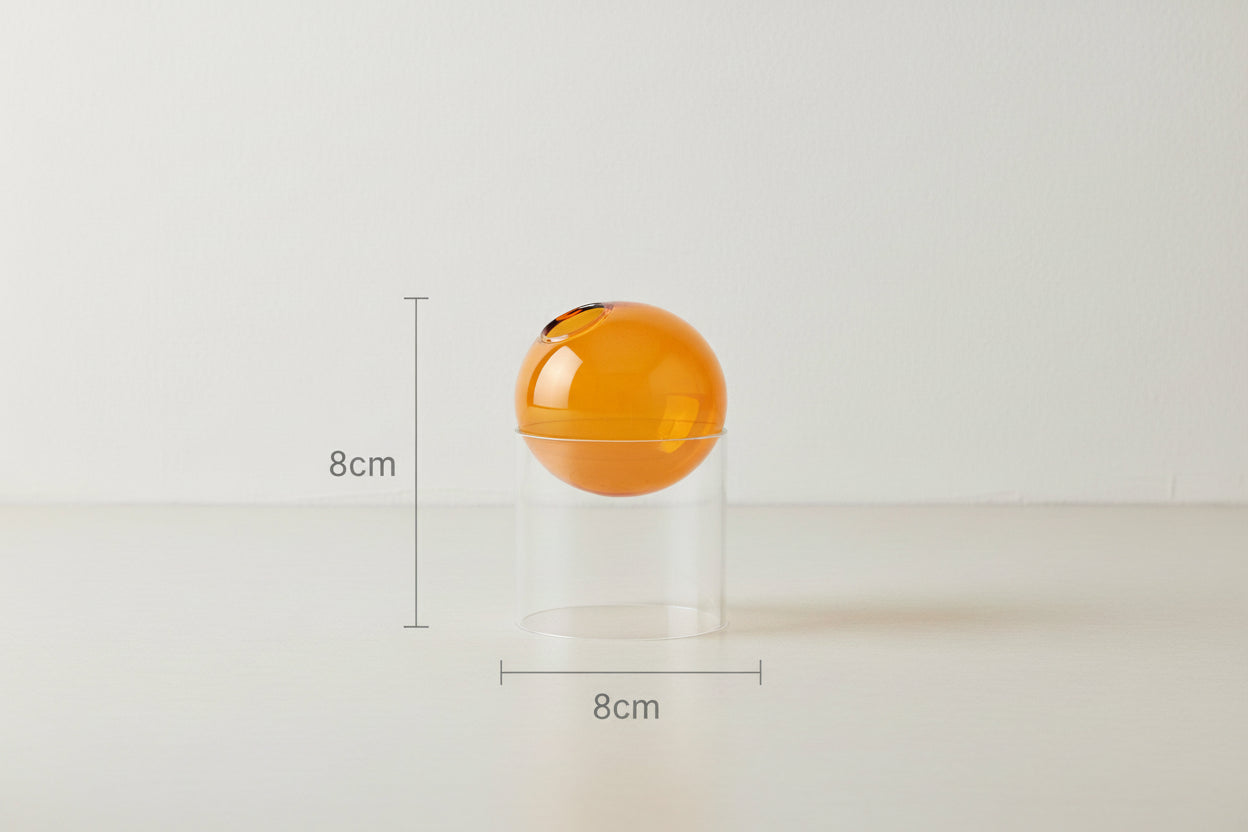 Orange spherical object inside a clear cylindrical container with dimensions labeled on a white background