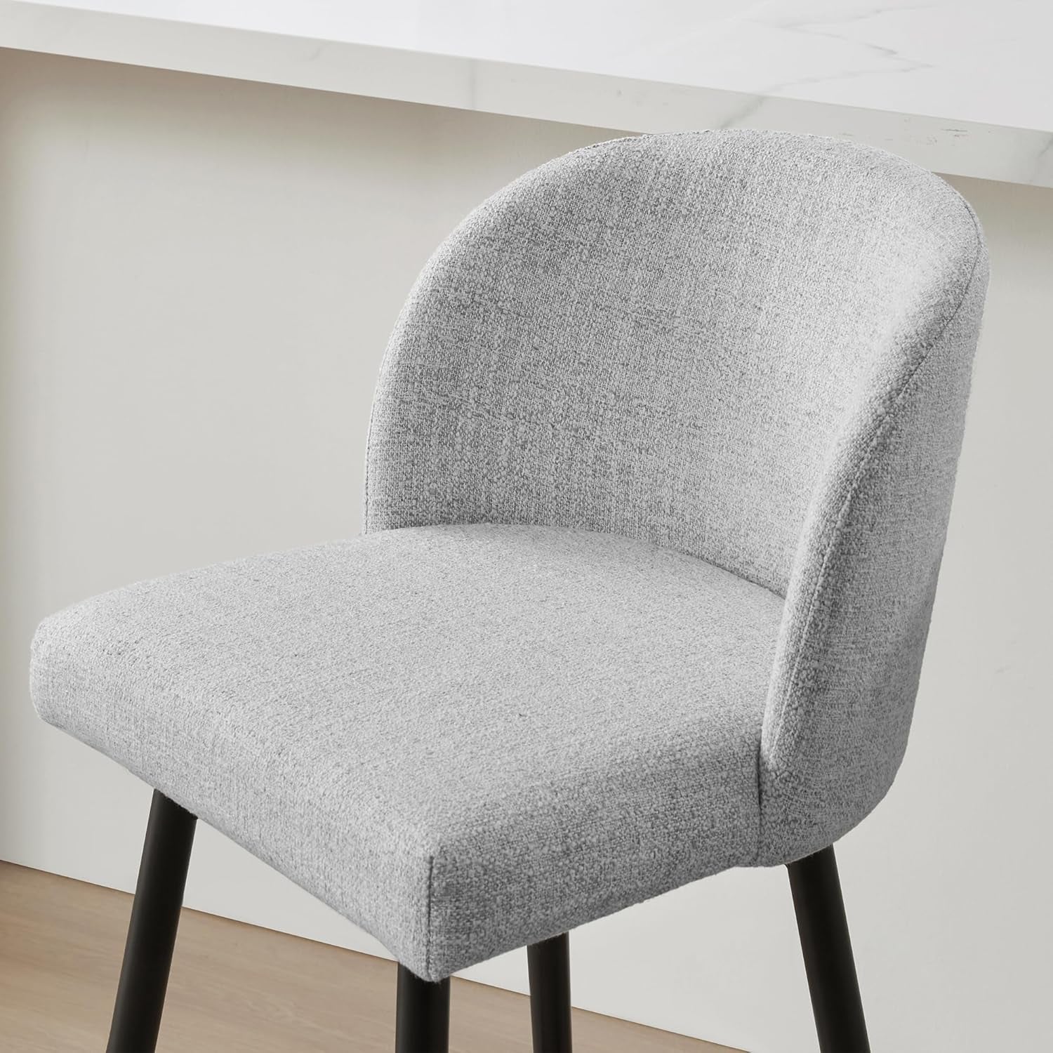 Gray upholstered chair with black legs against a white wall.