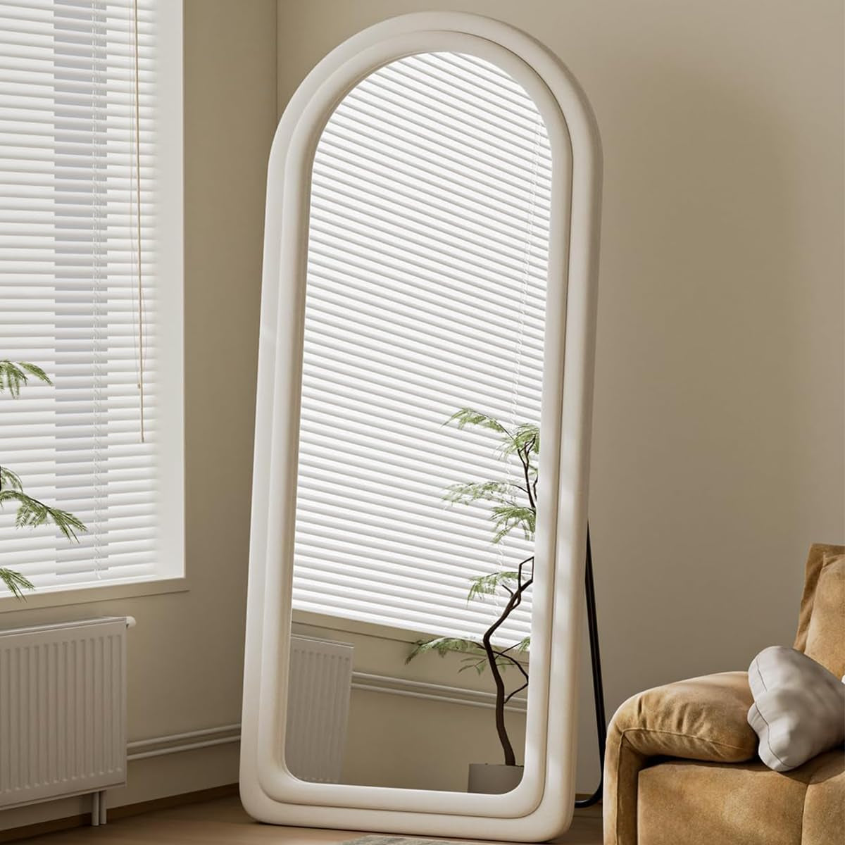 Large arched mirror with white frame leaning against a wall next to a window.