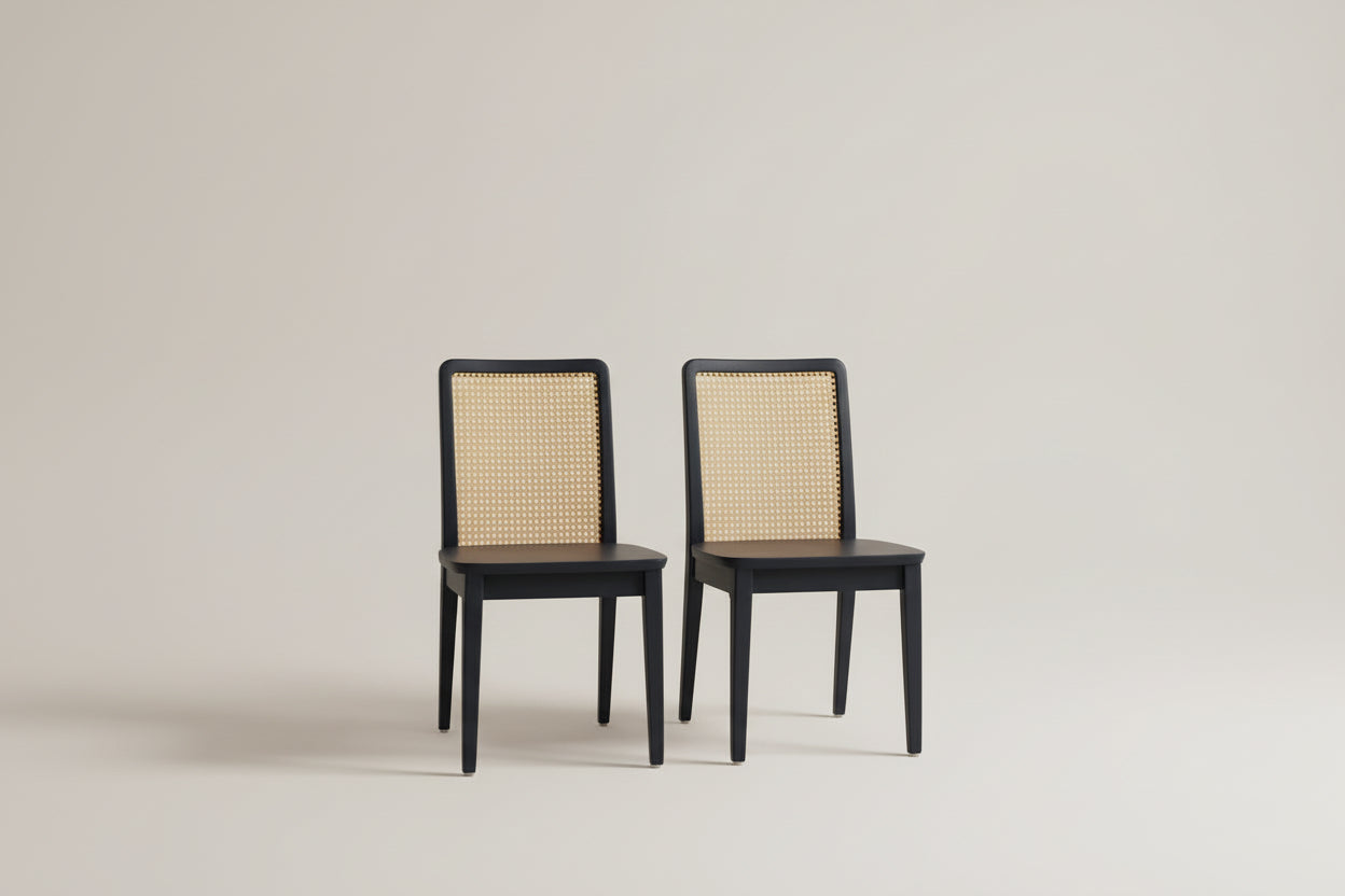Two black chairs with woven backrests in a room with a lamp and books on a table.