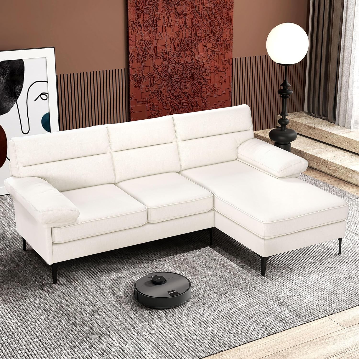 White sectional sofa in a living room with a robot vacuum cleaner on the floor.