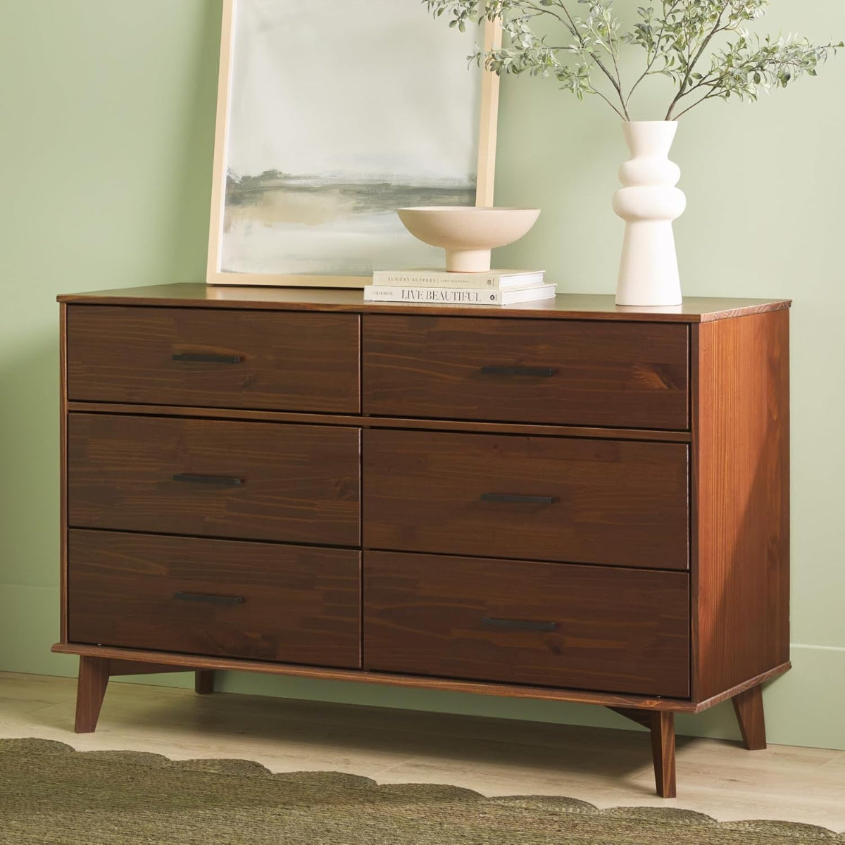 Wooden dresser with four drawers against a green wall with decorative items on top.