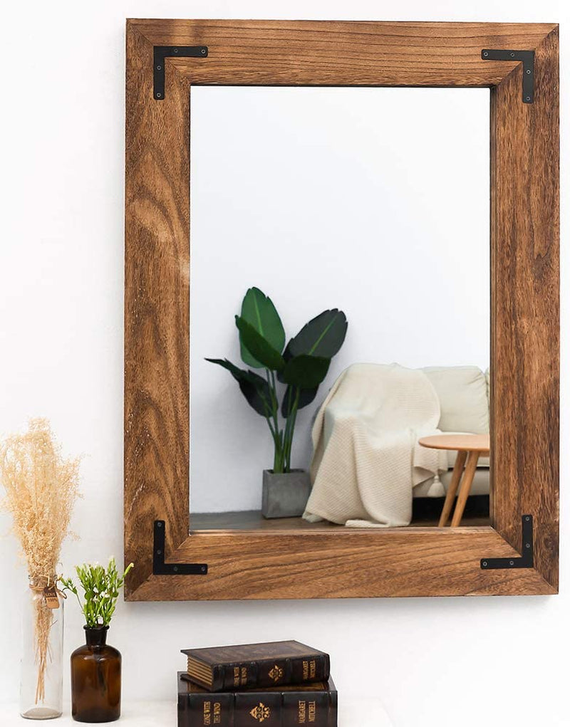 Wooden-framed mirror reflecting a plant and a sofa in a room.