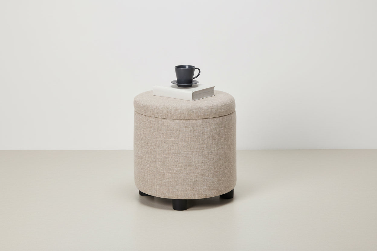 Round beige ottoman with a cup and saucer on top against a white background