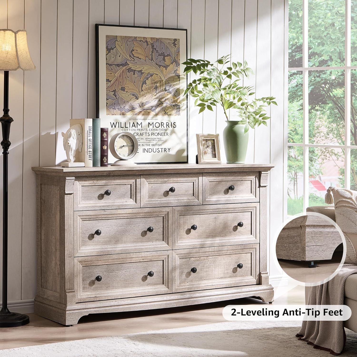 Wooden dresser with multiple drawers in a room with a lamp, plant, and framed picture.