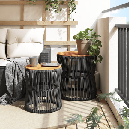 Two black woven side tables with wooden tops on a balcony with plants and cushions.