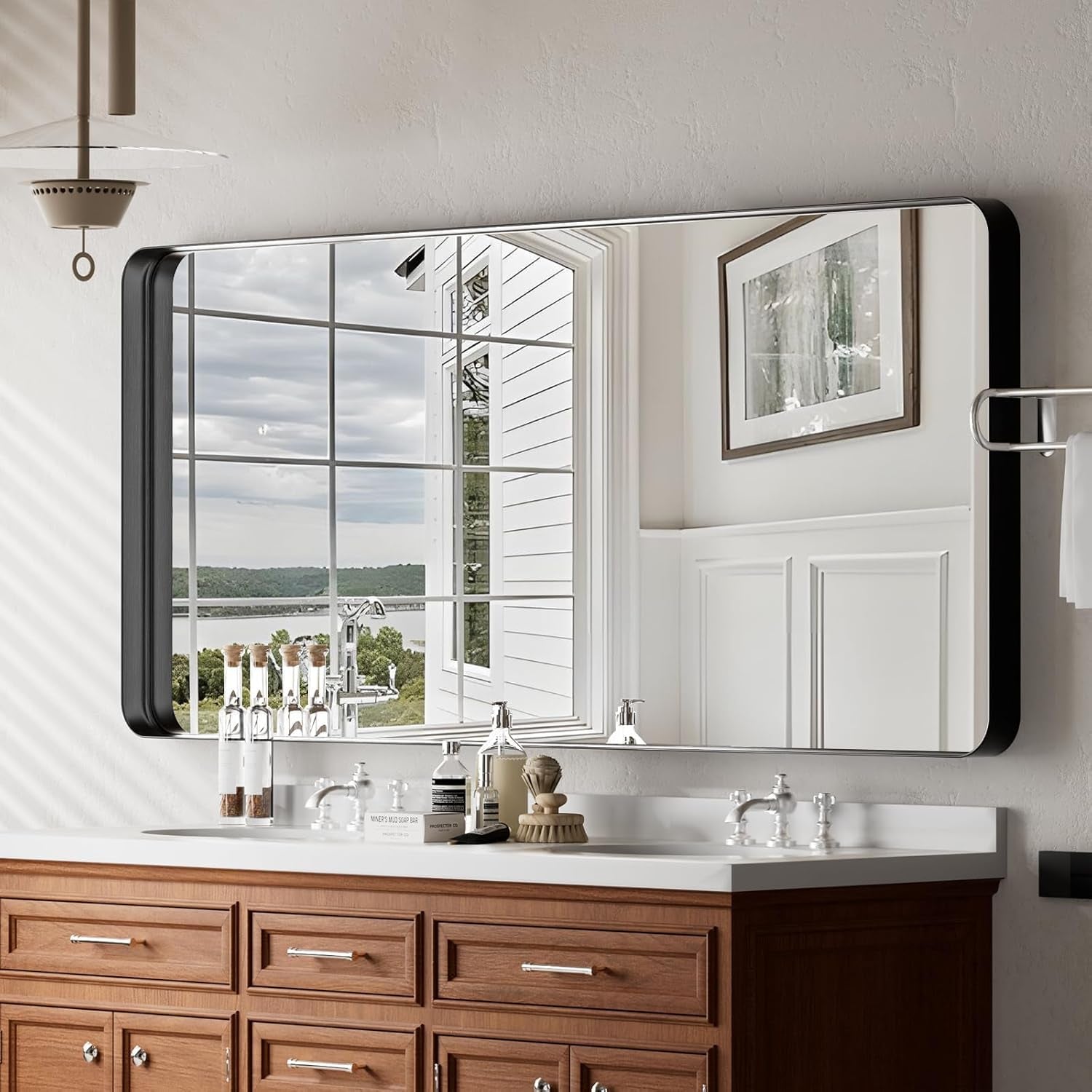 Bathroom vanity with large mirror reflecting a window view of trees and sky.