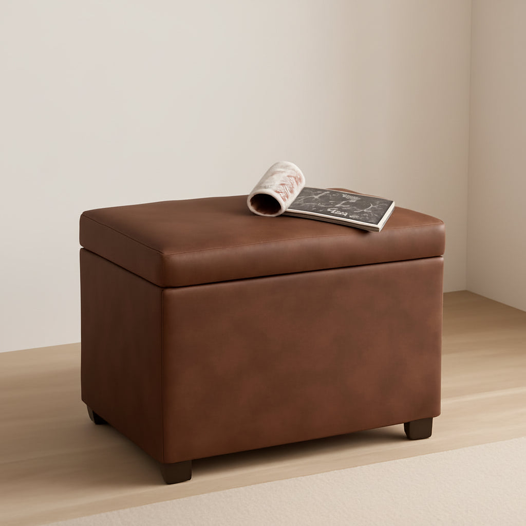 Brown leather ottoman with a book and magazine on top in a room setting.