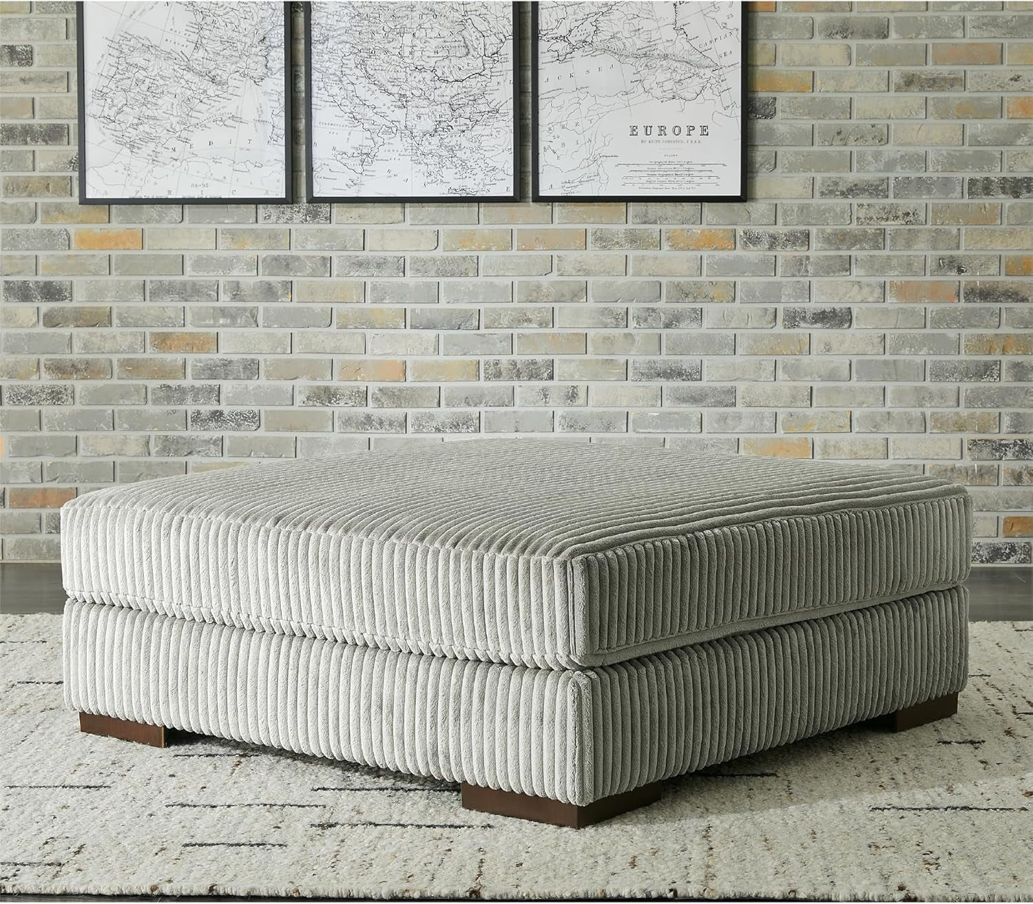 Gray ottoman against a brick wall with framed maps.