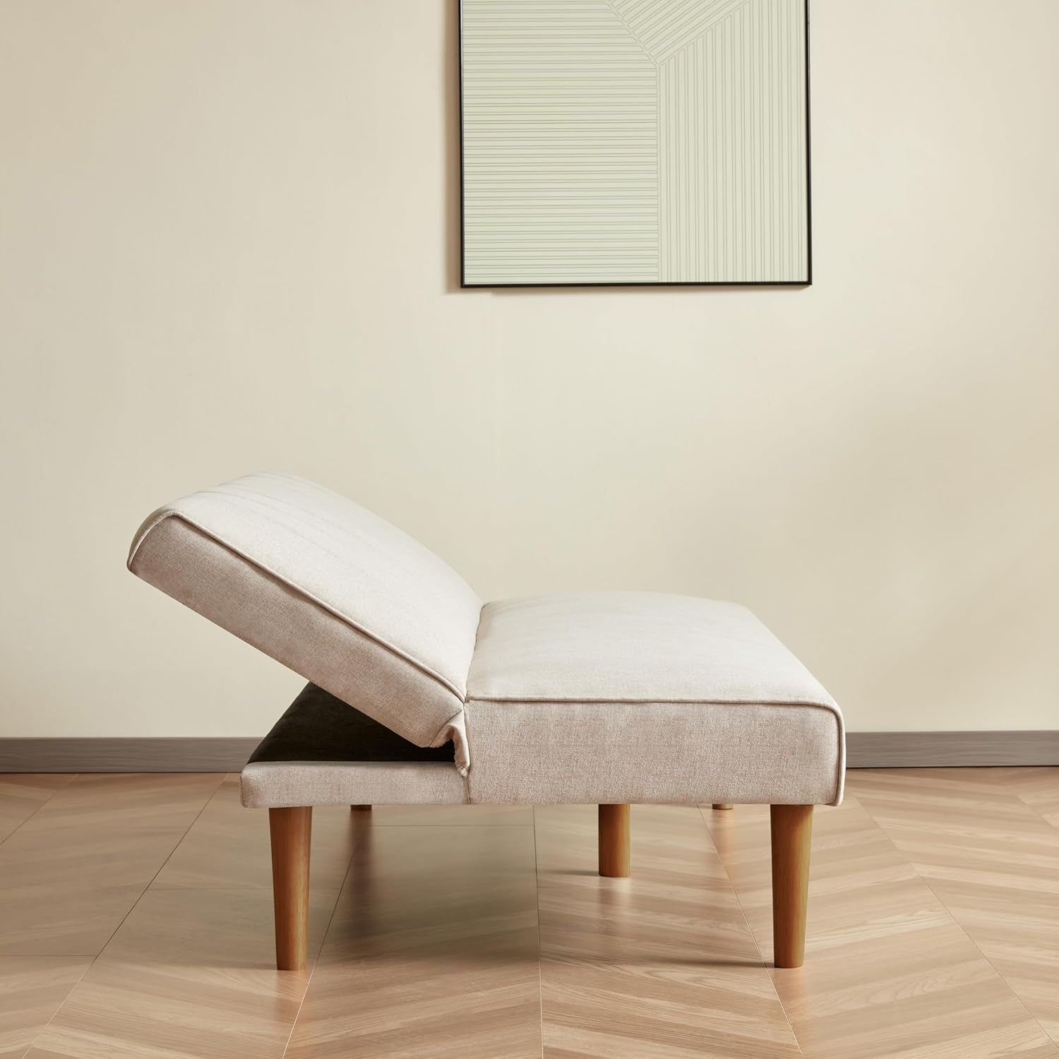 Beige ottoman with wooden legs in a room with a light-colored wall and wooden floor.