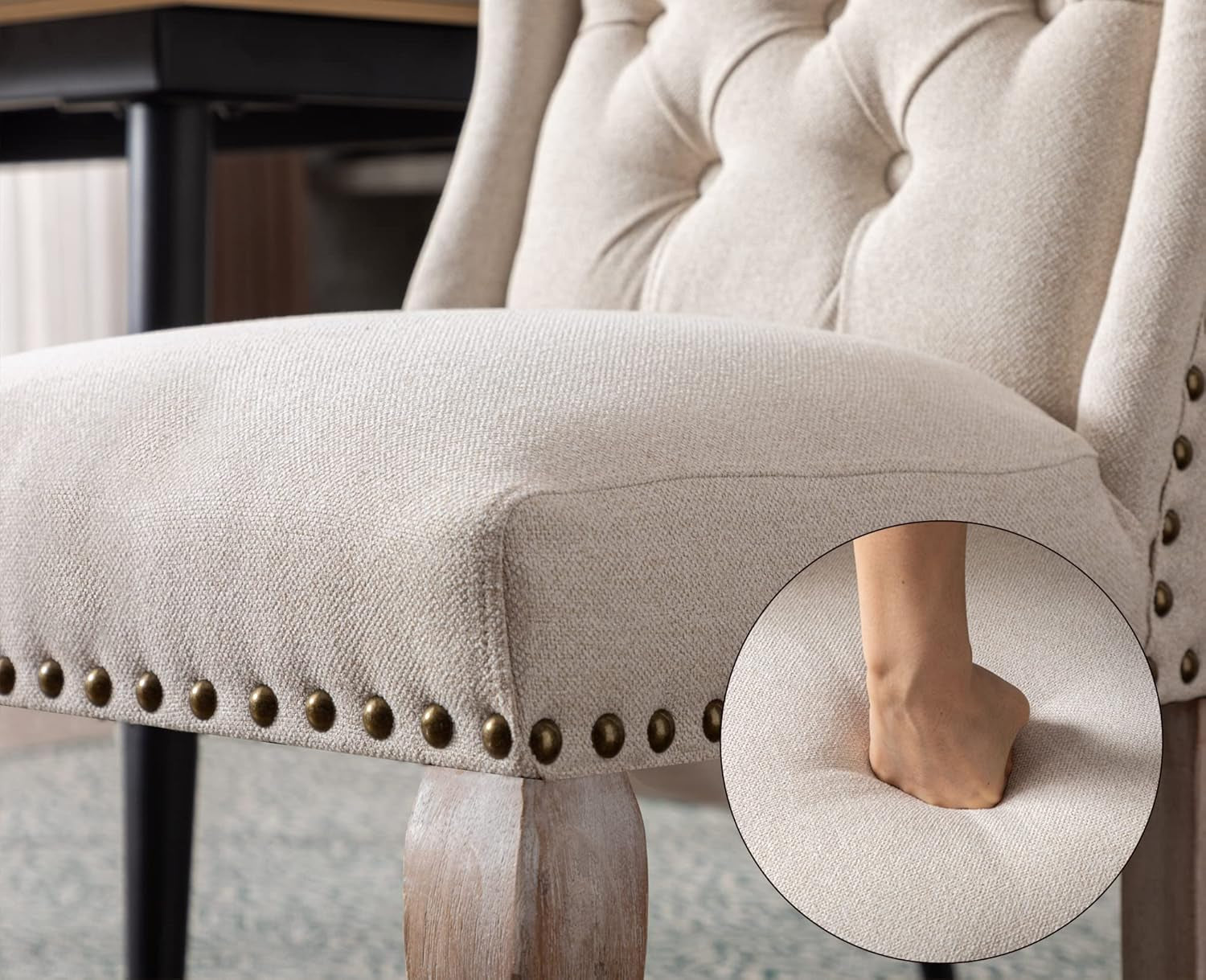 Close-up of a beige upholstered chair with studded details and a blurred foot on a carpeted floor.