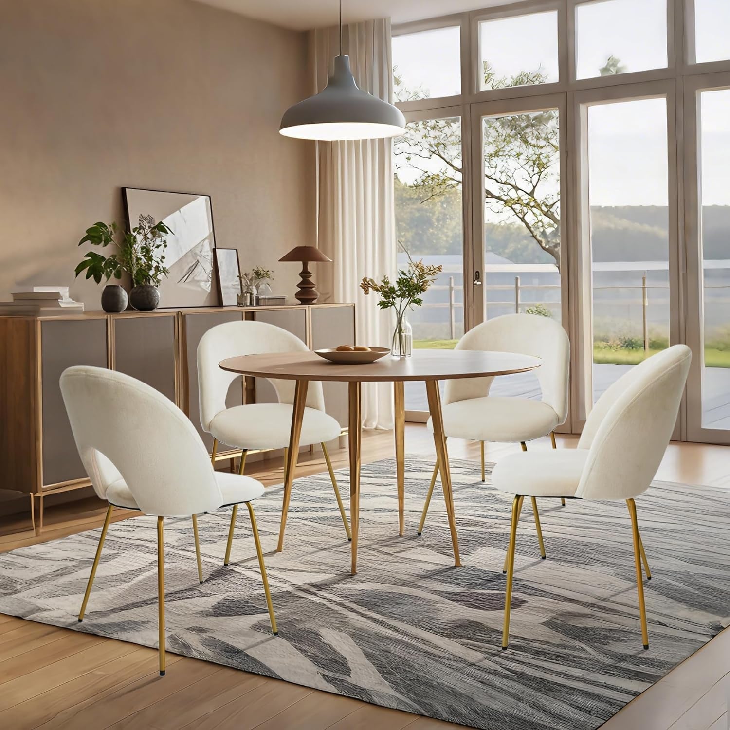 Dining room with a round wooden table and white chairs with gold legs, large windows overlooking a scenic view.
