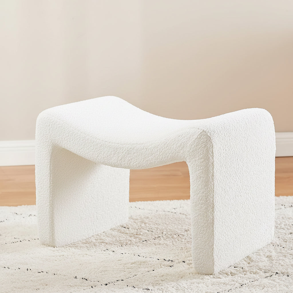 Person sitting on a white textured stool reading a magazine in a room with a neutral color palette.