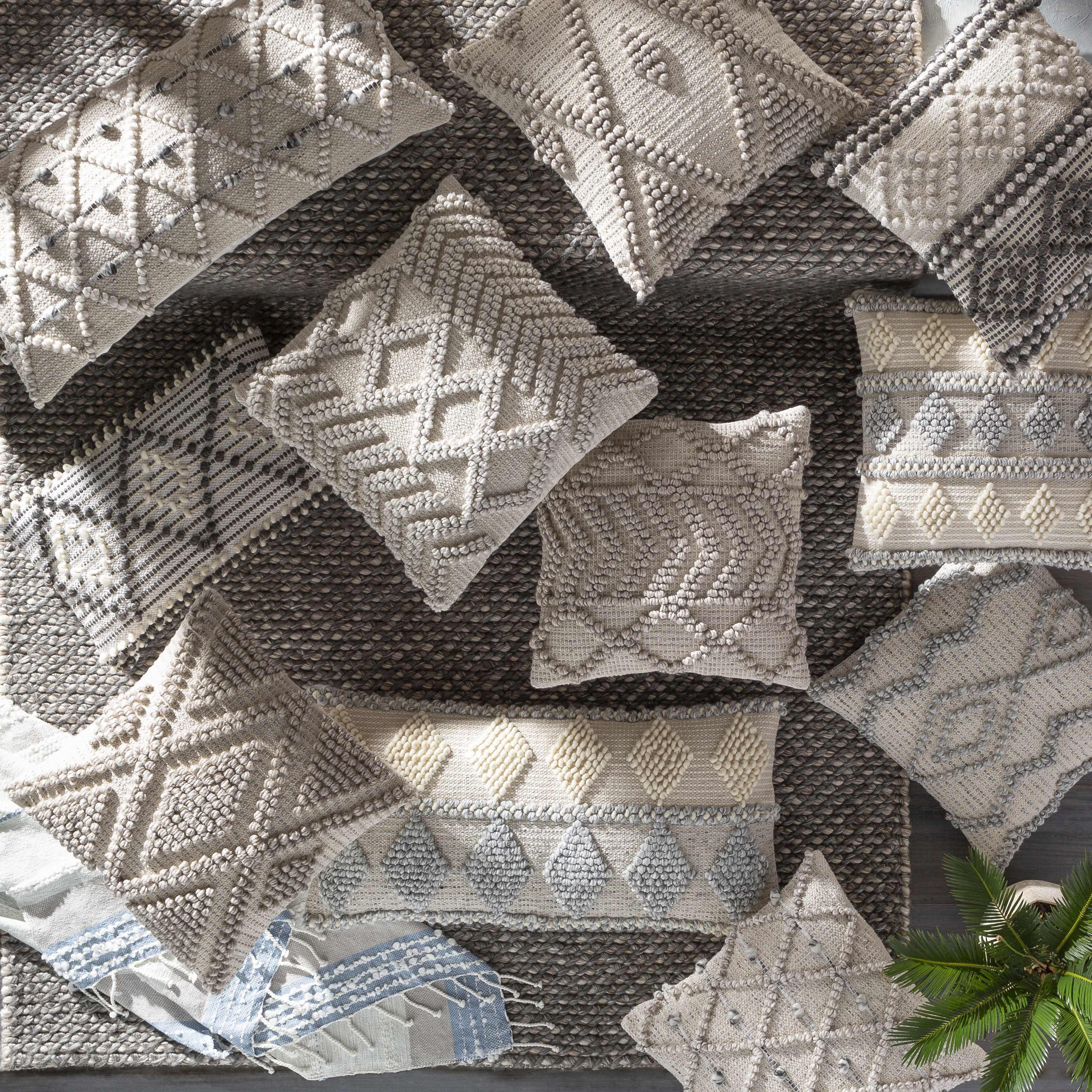 Collection of patterned cushions on a textured surface with a plant in the corner.