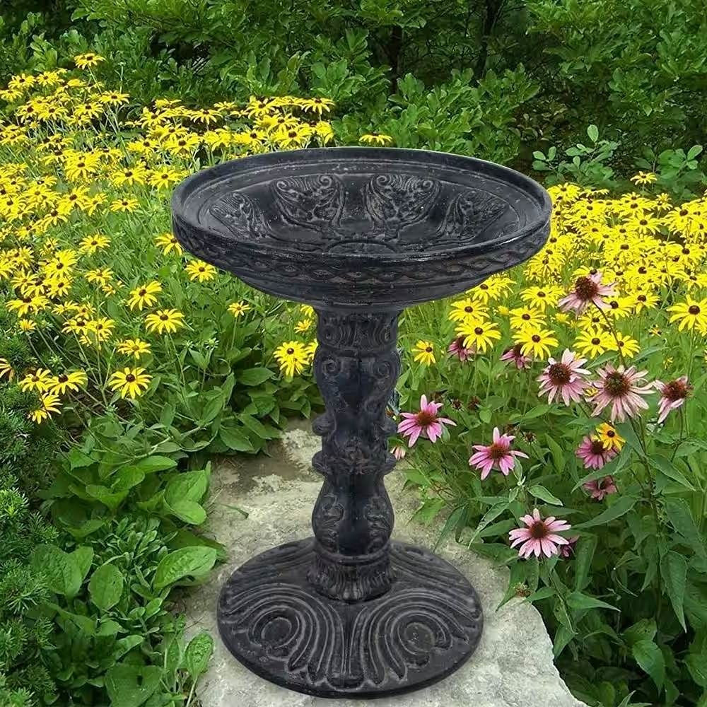 Decorative black bird bath surrounded by flowers in a garden setting