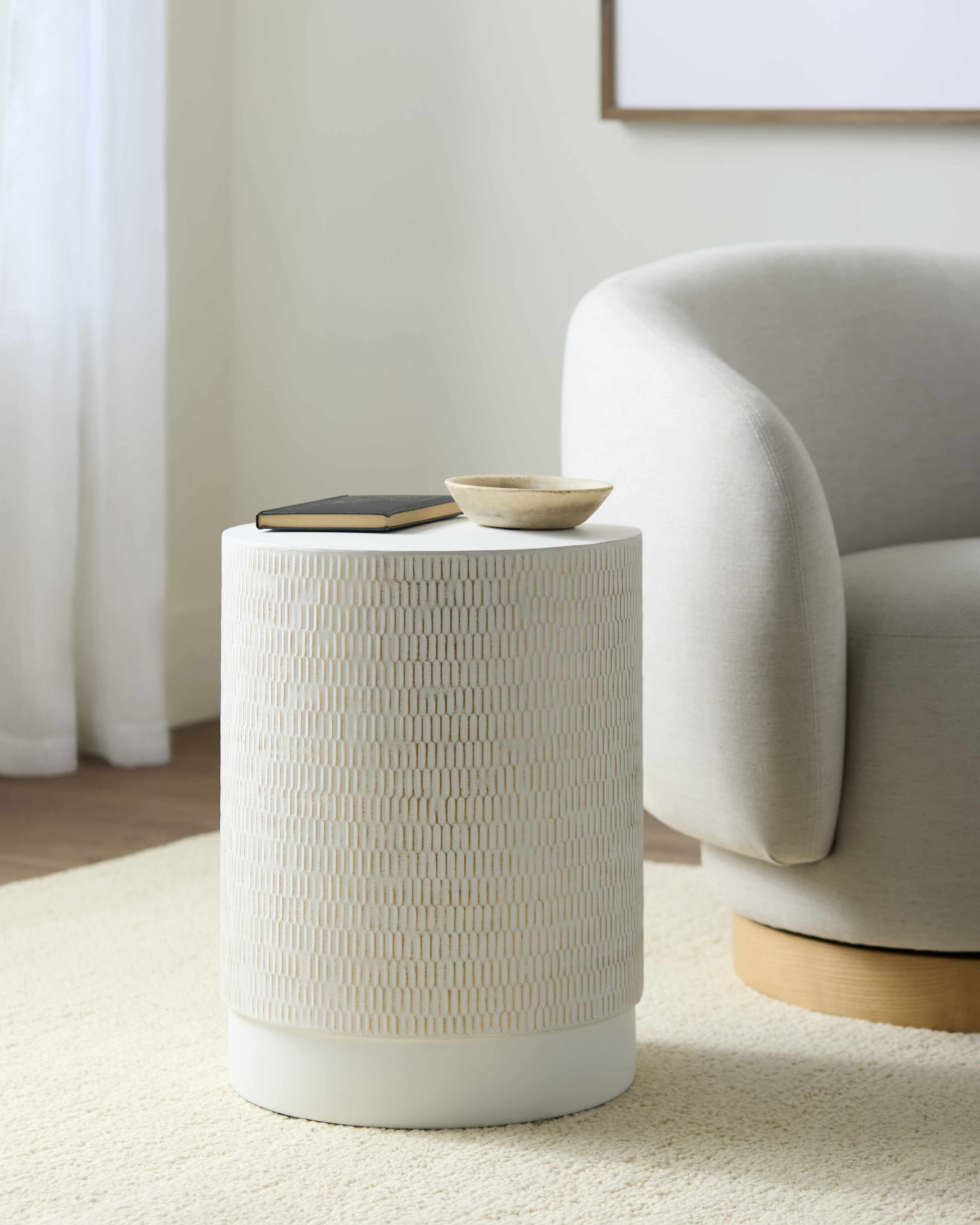 Textured side table in a modern living room with a chair and decor items.