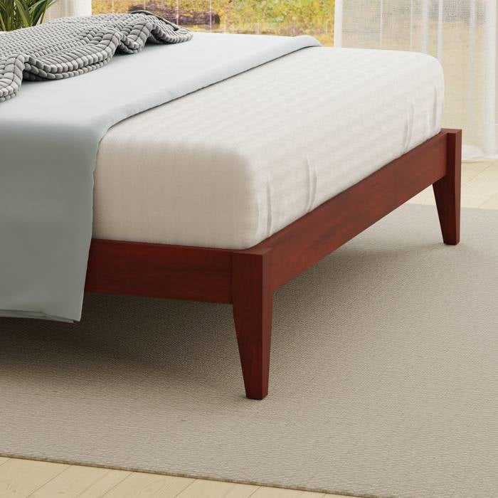 Wooden bed frame with white mattress and gray blanket in a room with light-colored carpet and curtains.