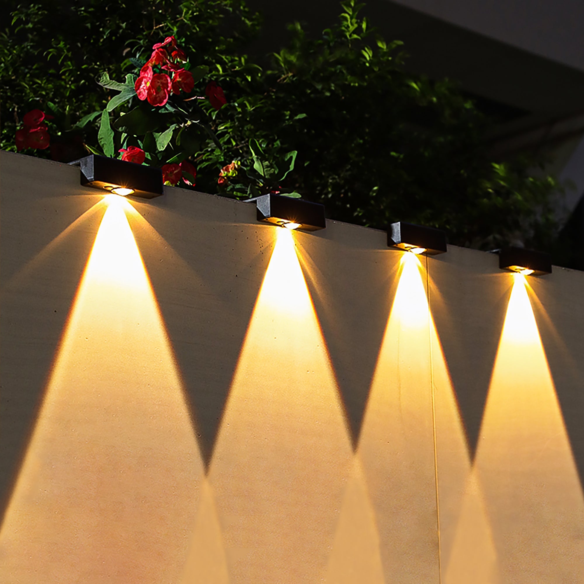 Row of outdoor lights on a wall with plants and flowers in the background