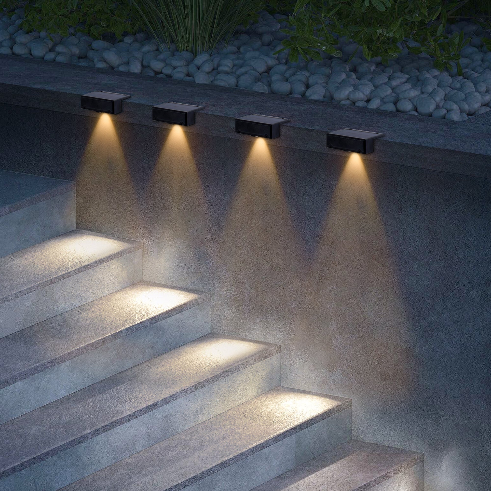 Outdoor steps illuminated by wall-mounted lights with a stone wall and pebbles in the background.