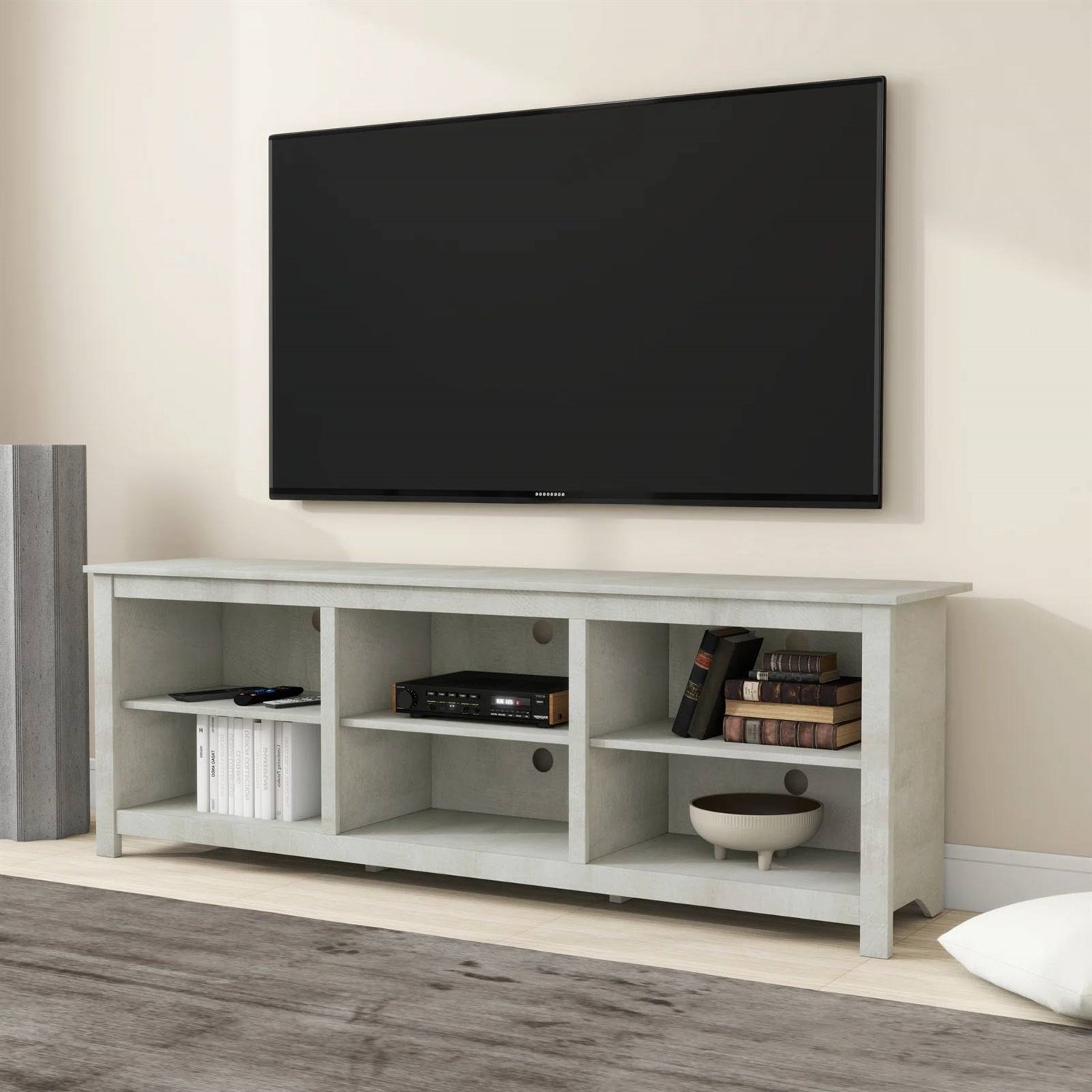 TV mounted on a wall above a light gray TV stand with electronic devices and books.