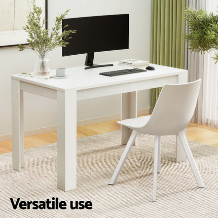 White desk with computer setup in a room with plants and curtains.
