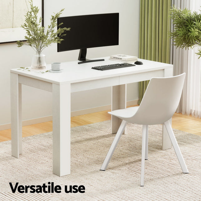 White desk with computer setup in a room with plants and curtains.