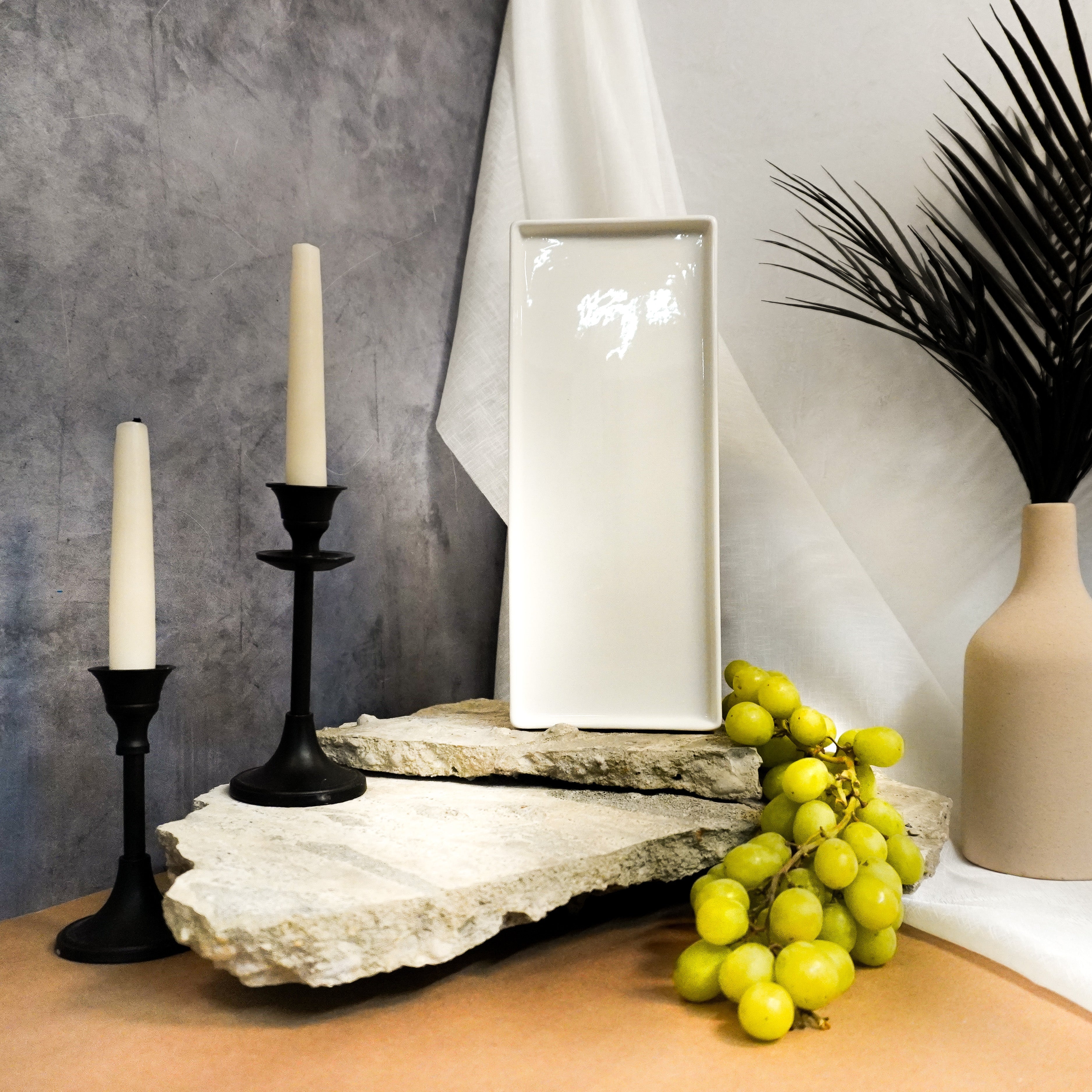 Decorative setting with candles, a vase, and grapes on a surface.