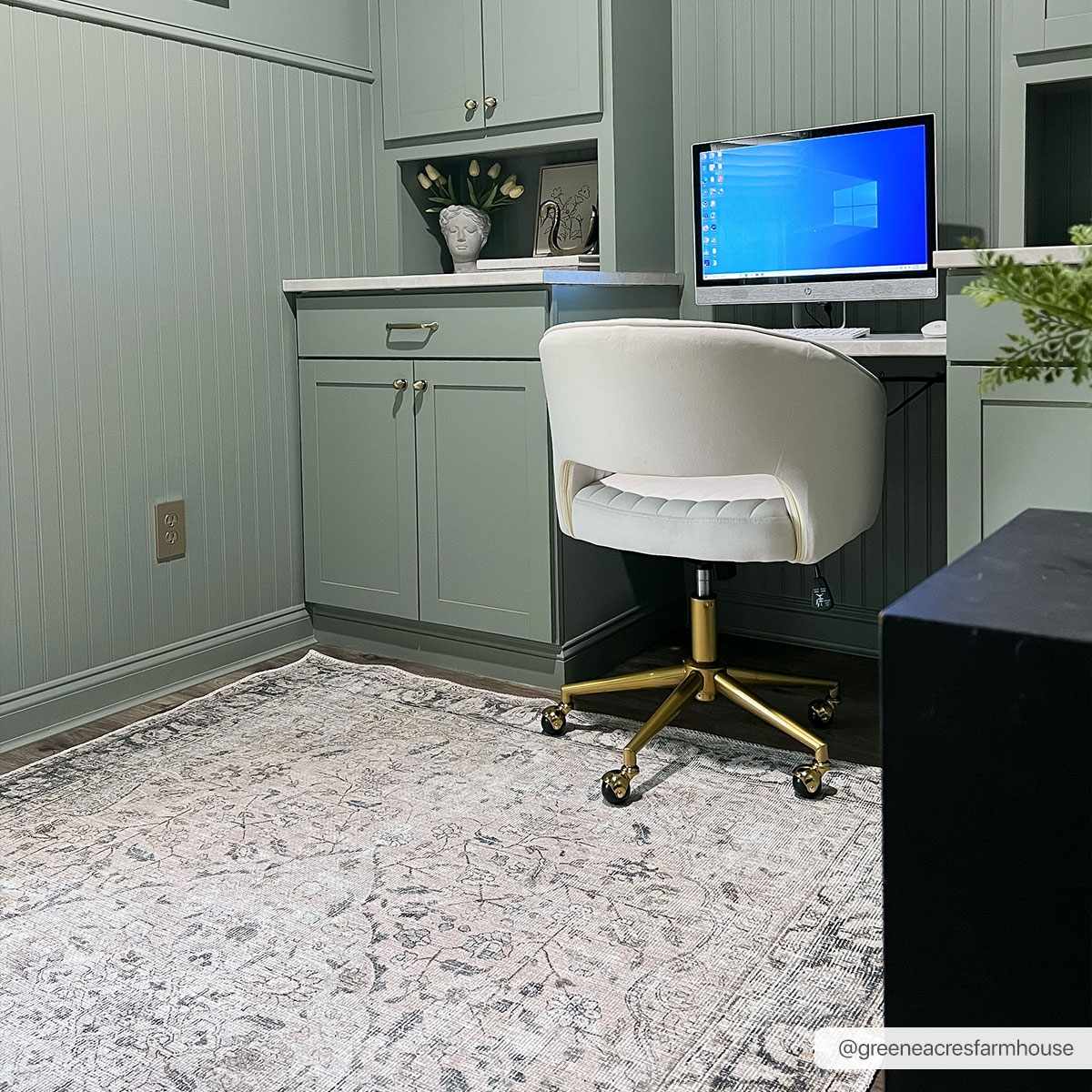 Home office with a desk, chair, and computer monitor in a room with gray walls and a patterned rug.
