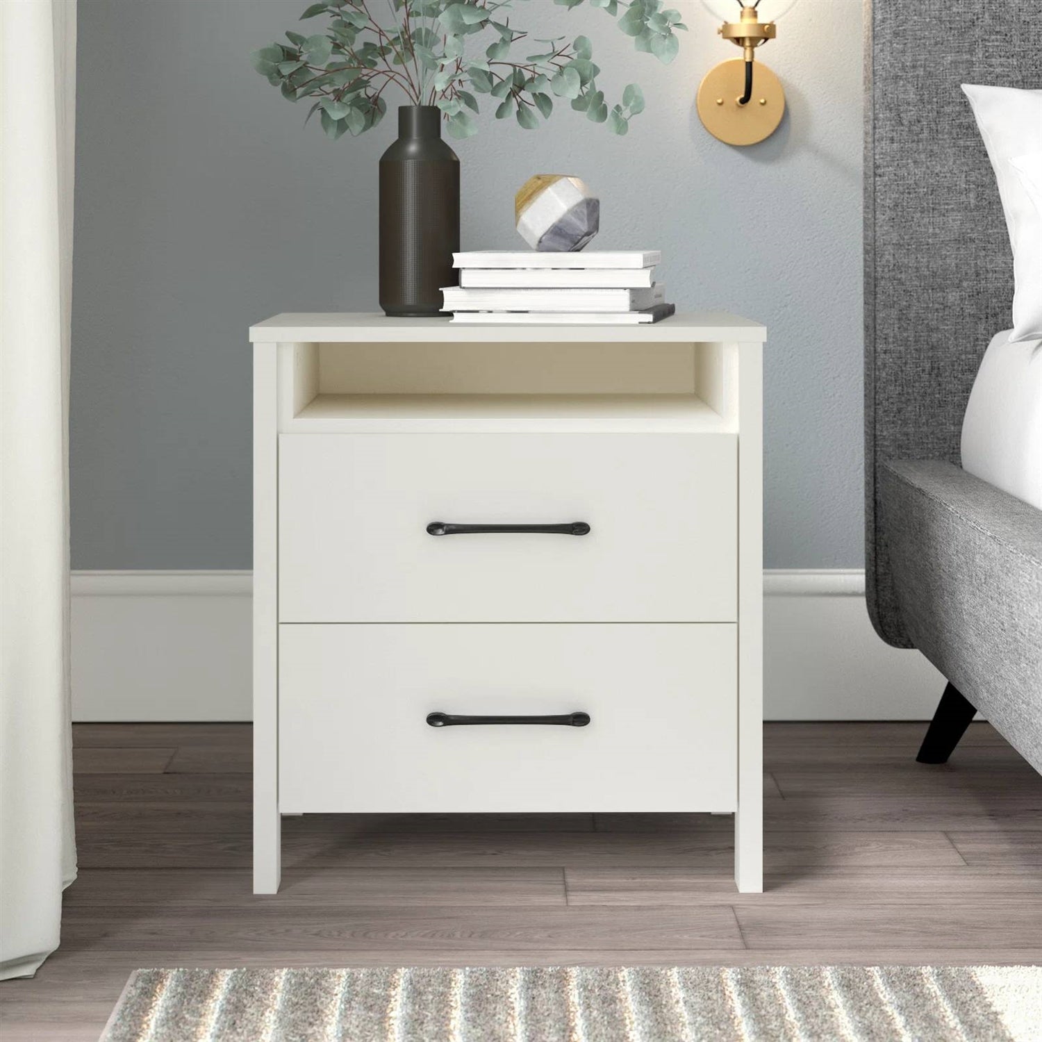 White nightstand with two drawers, books, and a vase in a bedroom setting.