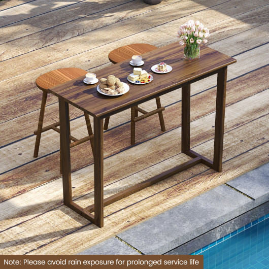 Wooden outdoor table with food and flowers on a wooden deck by a pool.