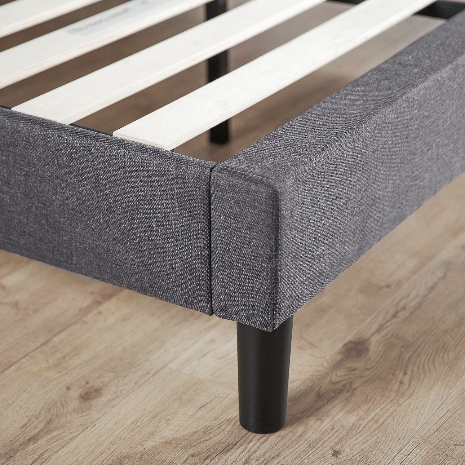 Gray upholstered bed frame with wooden slats on a wooden floor