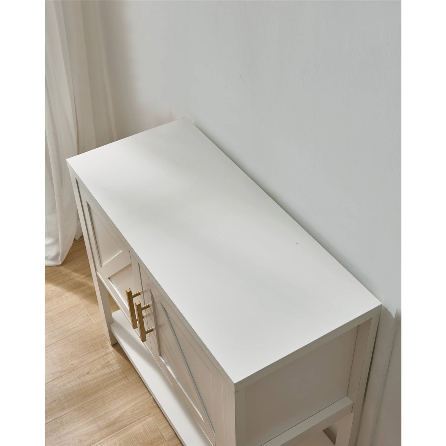 White cabinet with a gold handle on a wooden floor against a white wall